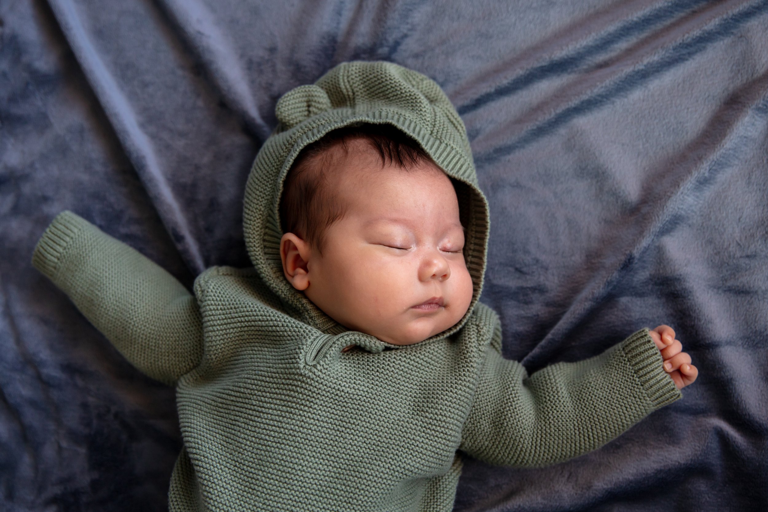 Close up of baby sleeping in a onesie with bear ears on the hood while laying on a blanket.