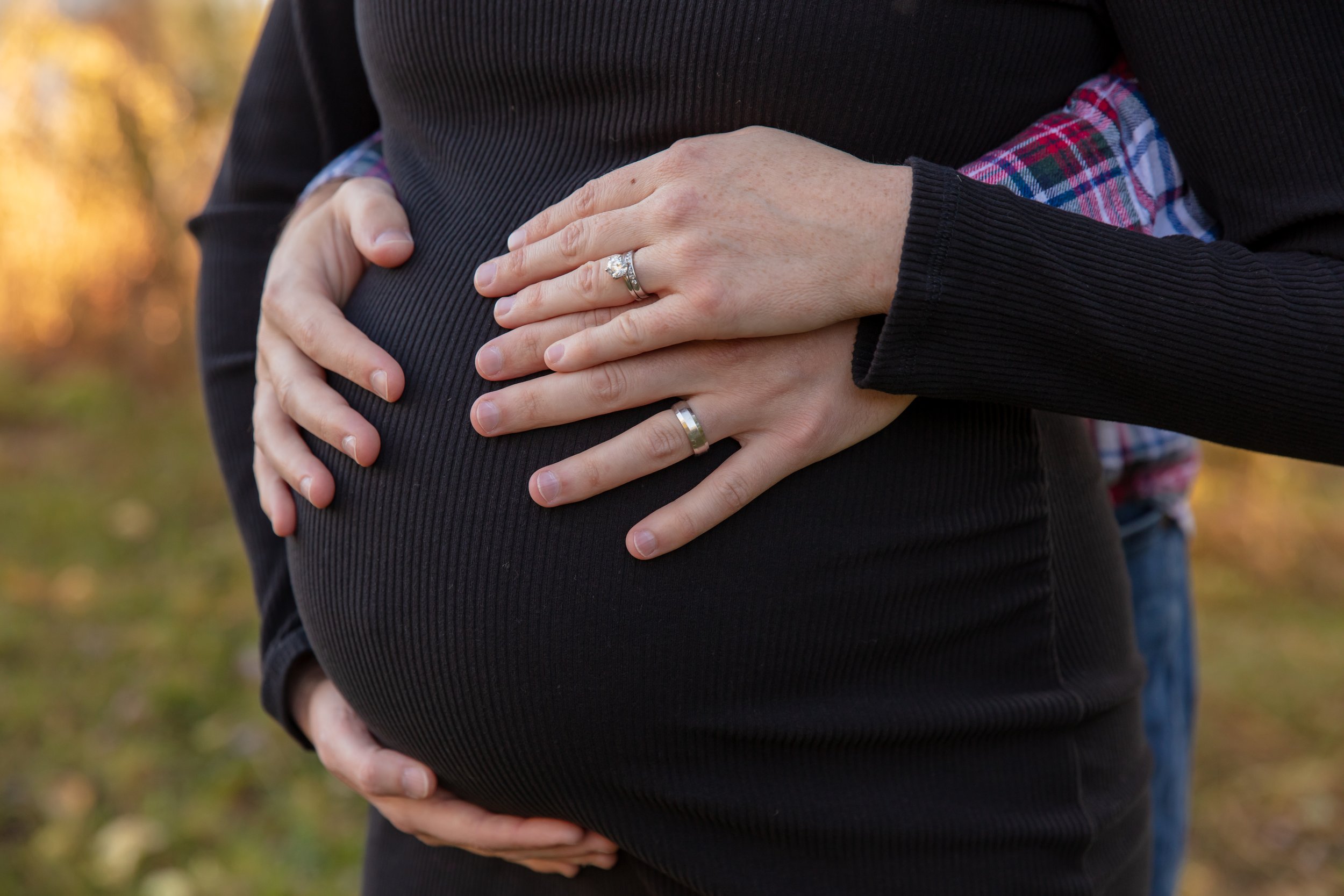 Maternity session, close-up image of expecting mother's baby bump with the hands of the mother and father-to-be cradling it.