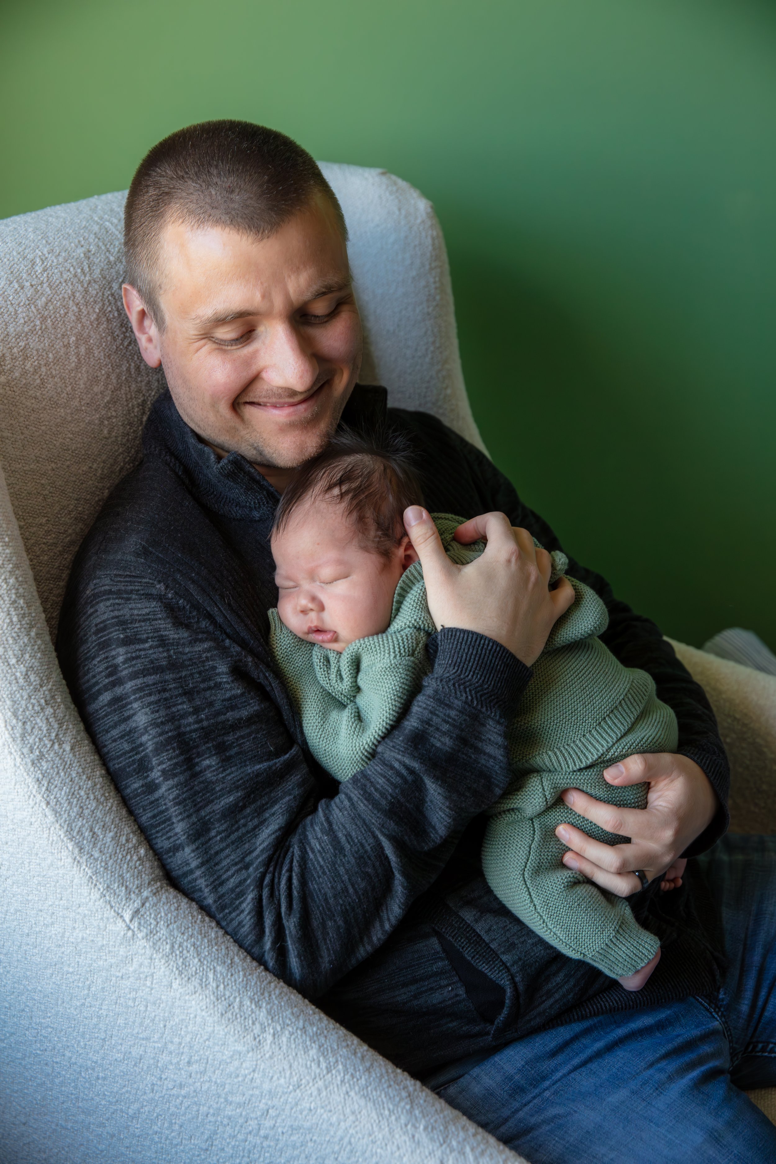 Dad holds his baby in his arms as he smiles down at his baby.