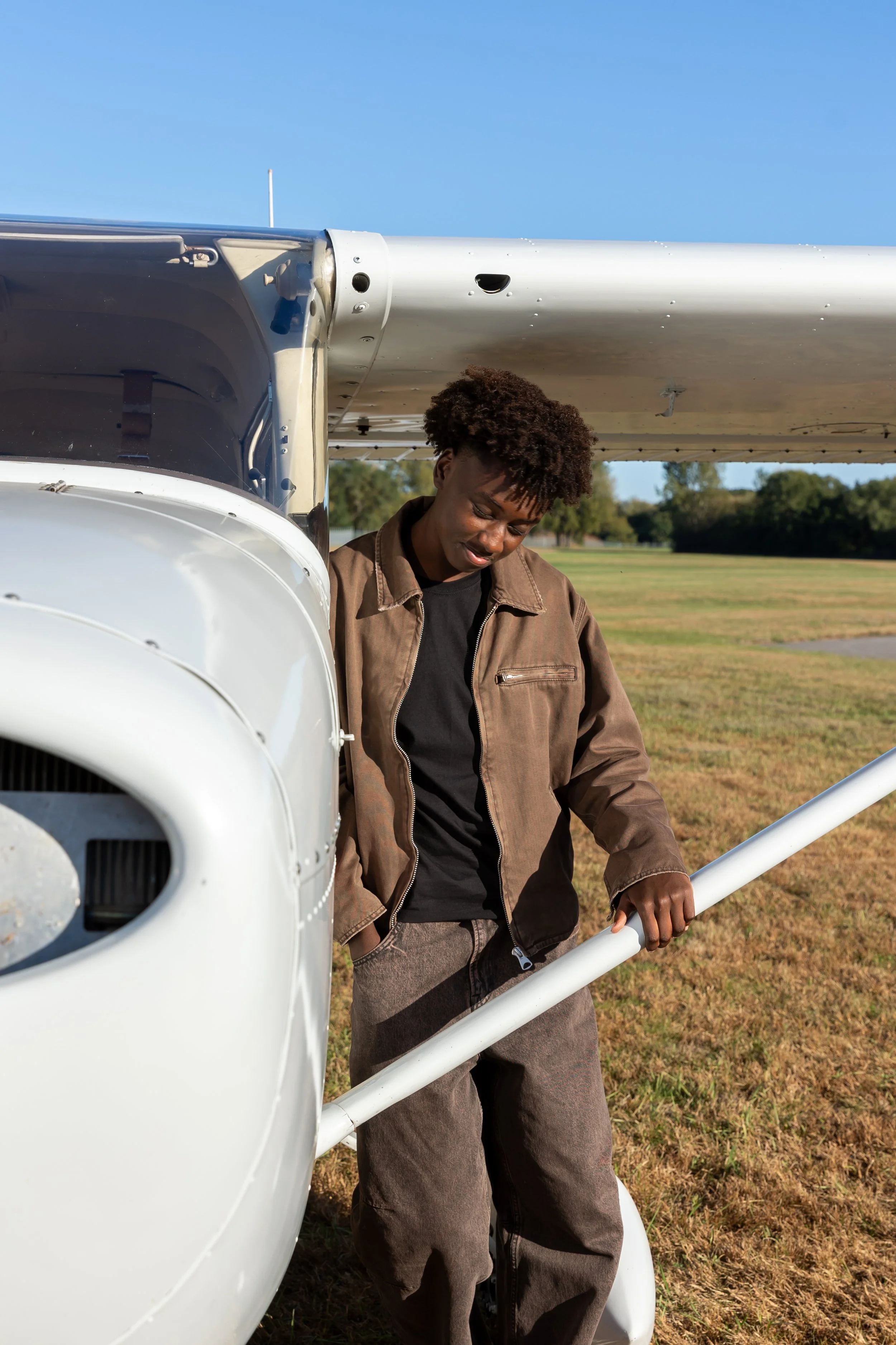 A Maple Grove high school senior stands against a Cessna airplane in the Crystal airport casually looking at the ground for their senior photos.