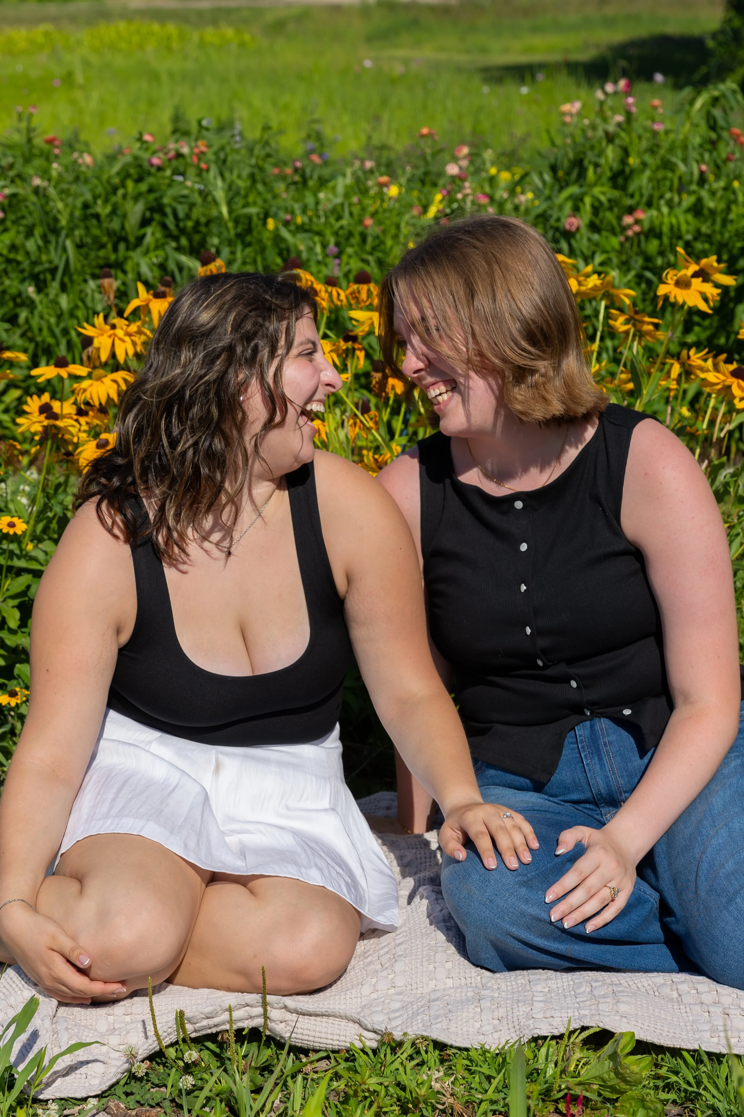 Minneapolis couples photography - A couple sits on a blanket together in front of daises smiling at each other at Lakeside Farm and Flowers in Cologne, MN.