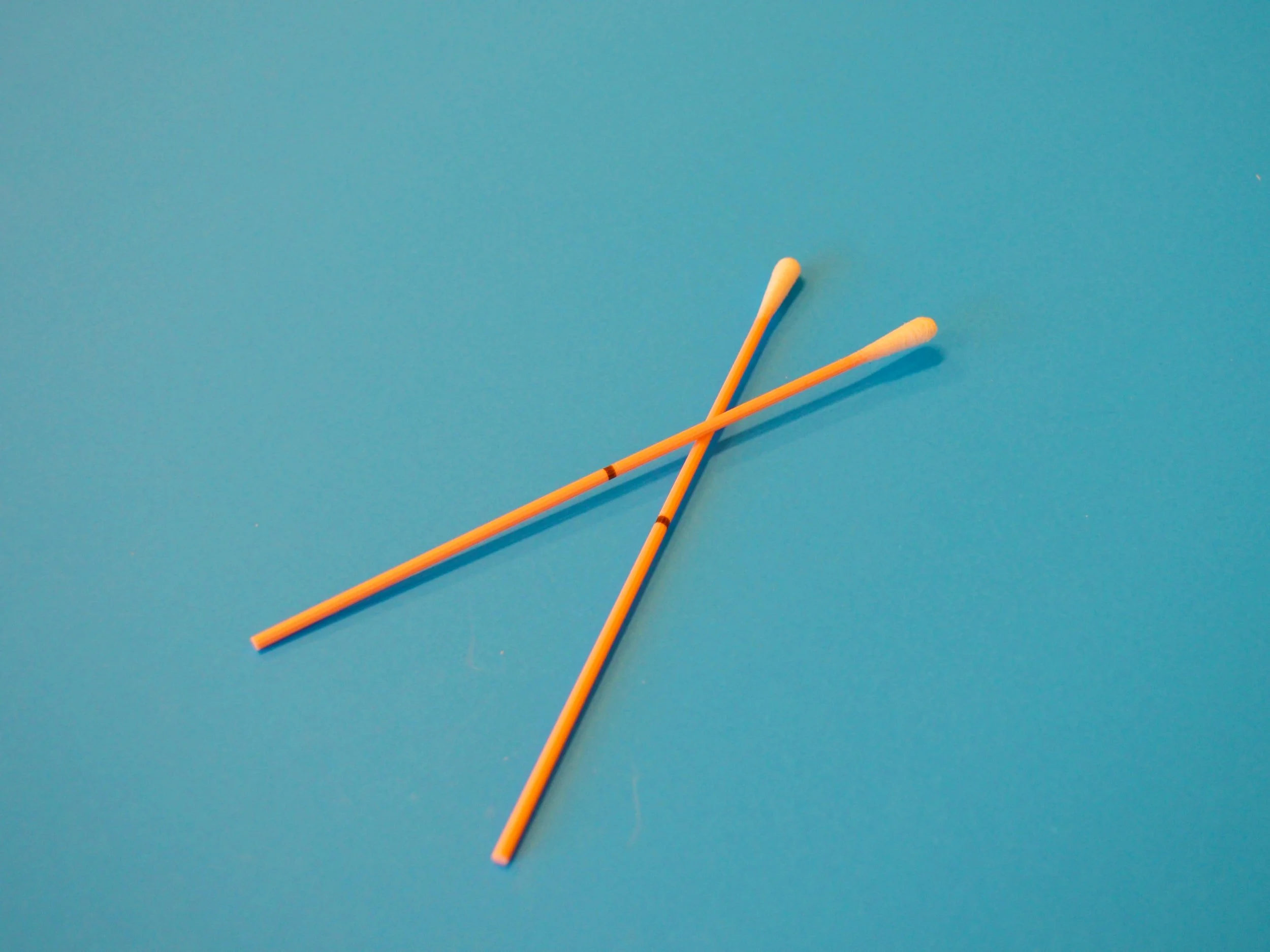 Two crossed cotton swabs with wooden sticks on a blue background.