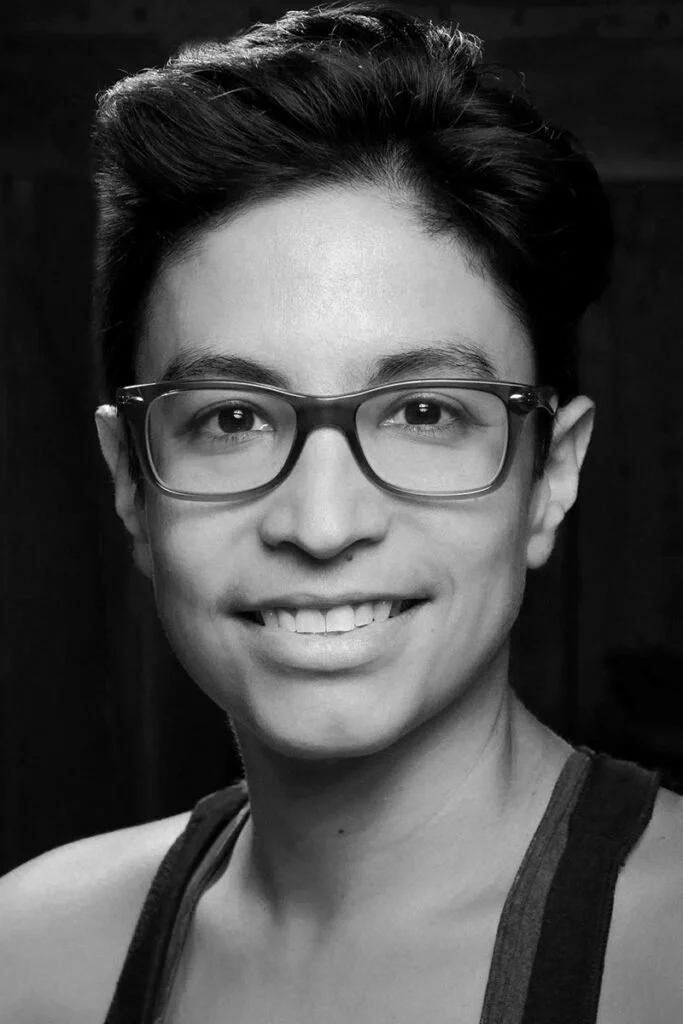Black and white portrait of a person wearing glasses and smiling with short hair.