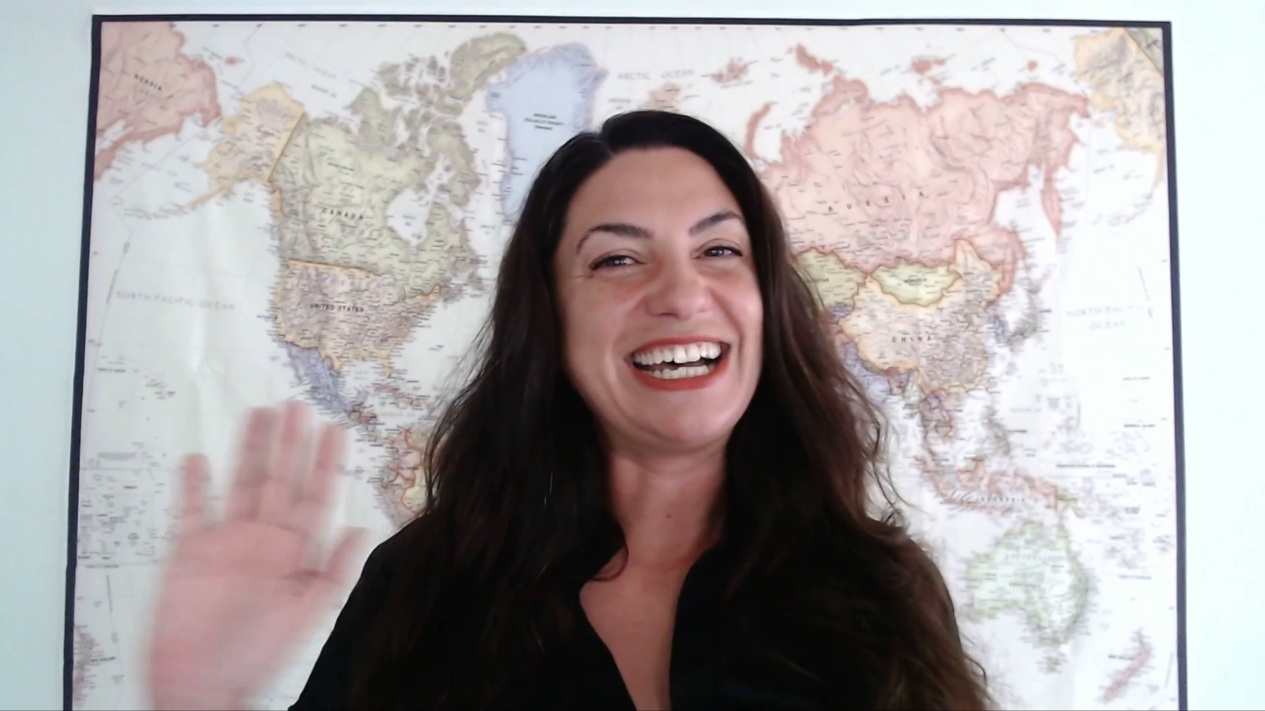 Course teacher Rocío Gómez-Aleixandre smiling in an intro video lesson of Spanish Uncovered Advanced, in front of a world map.