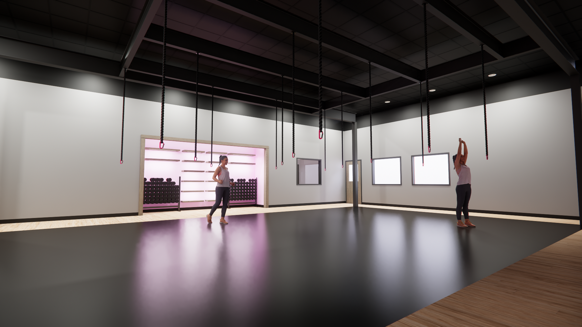 Inside a fitness or yoga studio with two women, one stretching and one standing, surrounded by hanging ropes from the ceiling, with wall shelves and dumbbells in the background.