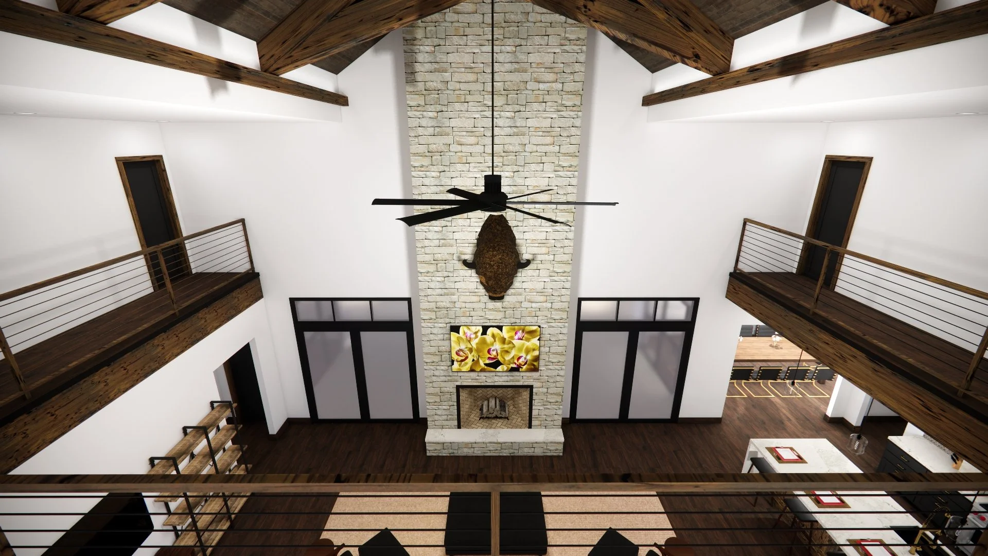 A spacious modern living room with a high ceiling, exposed wooden beams, a stone fireplace with a mounted animal, a ceiling fan, and a framed artwork of yellow flowers above the fireplace. There are large windows and balconies on either side.