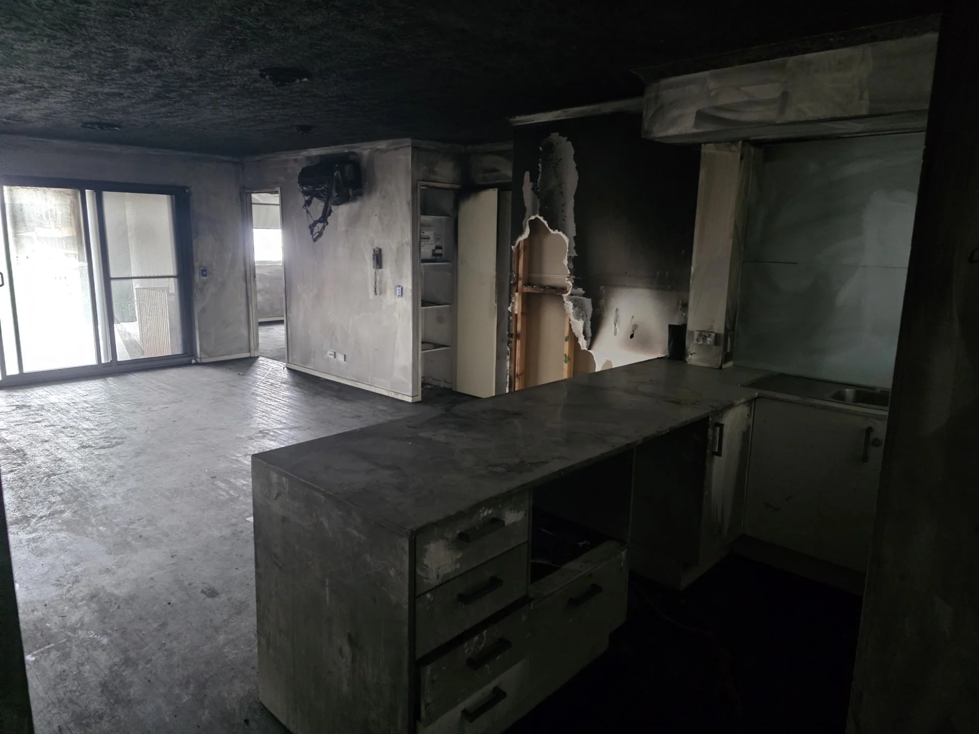 Room with burnt ceiling, damaged walls, and missing cabinetry, indicating fire damage.