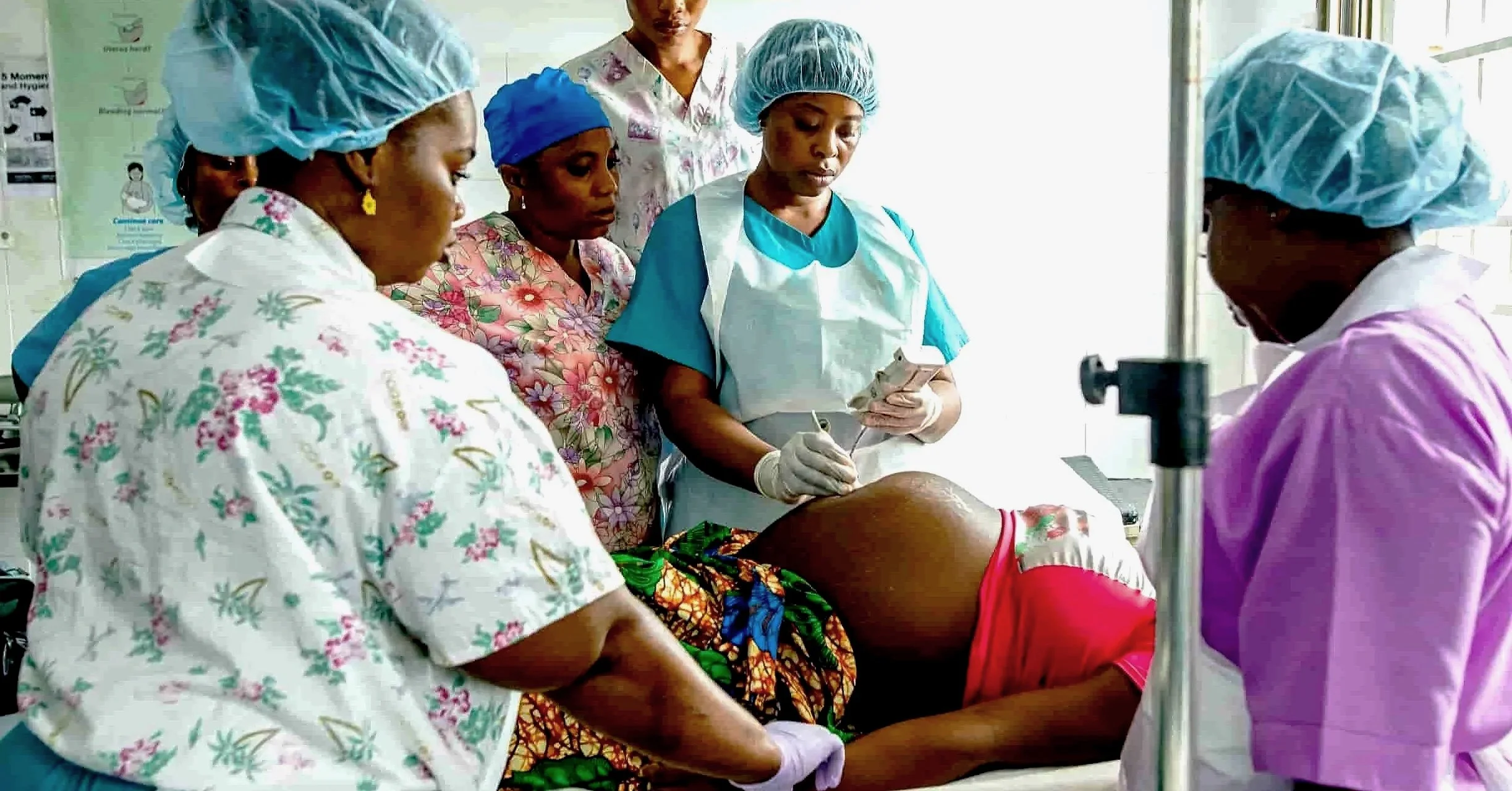 Healthcare team performs a childbirth delivery in a hospital setting with medical staff attending to a pregnant woman on an examination table.