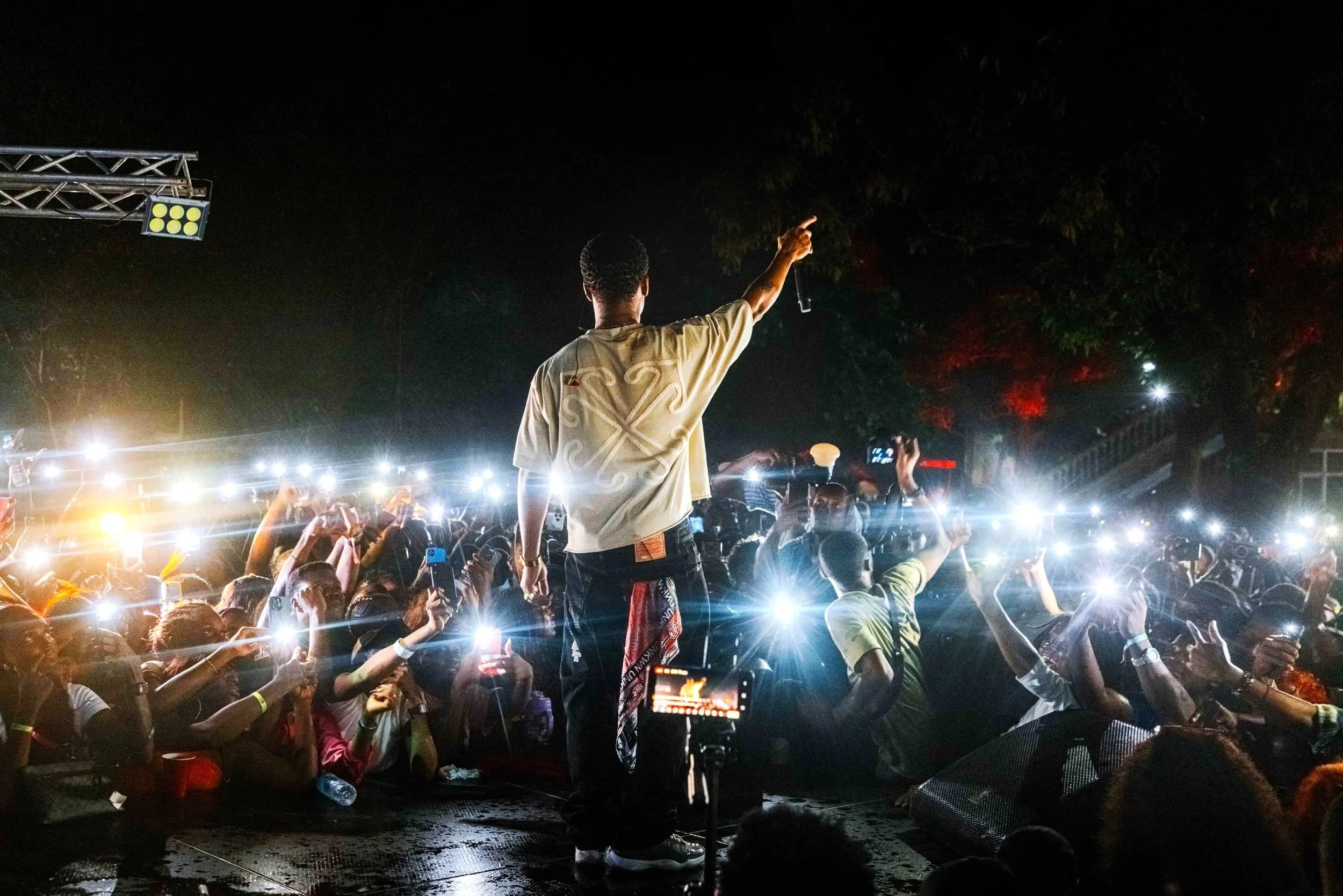 Performer on stage with audience holding up phones at nighttime outdoor concert.
