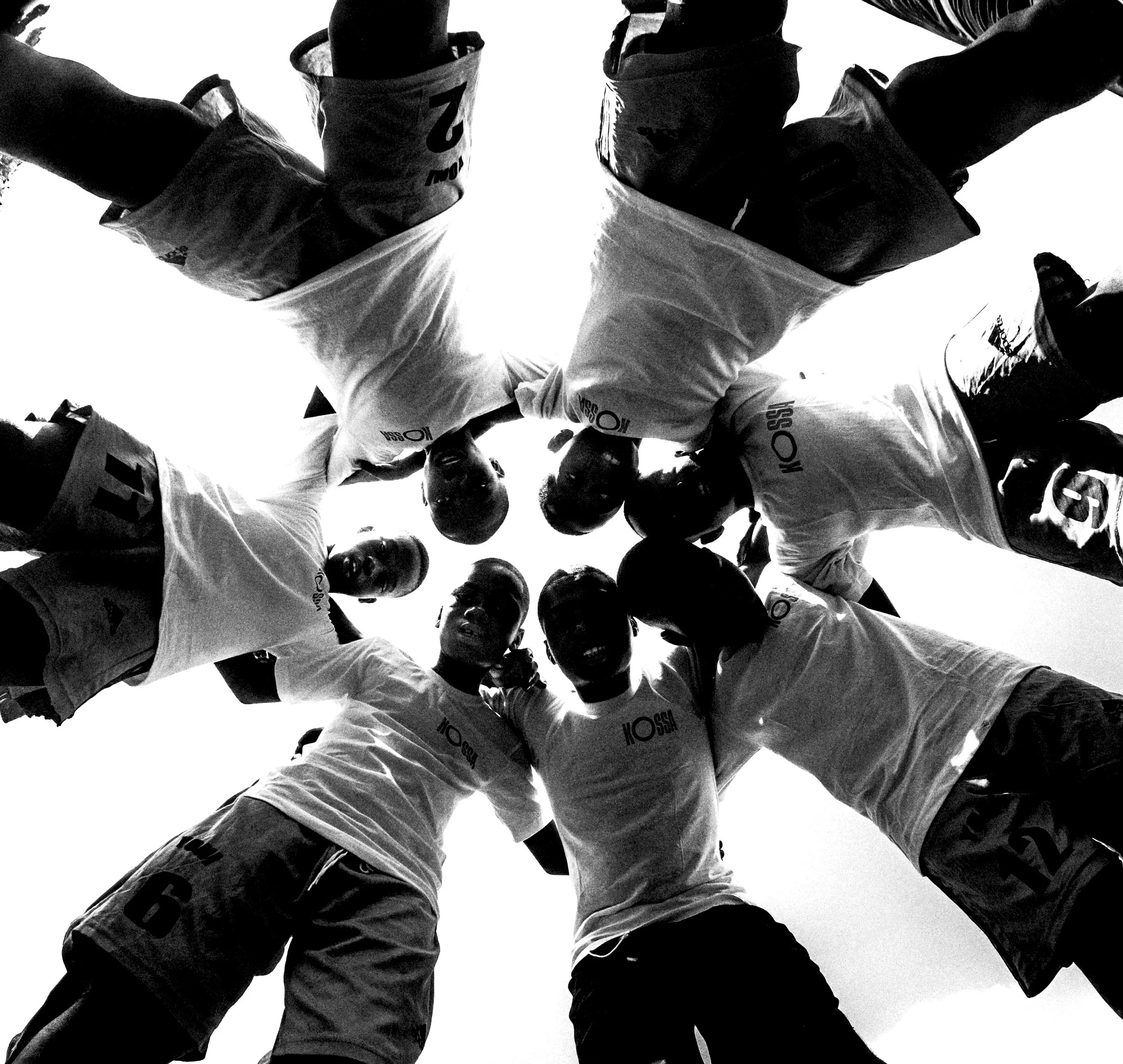 A black and white photo of a group of people standing in a circle taken from below, looking up at them.