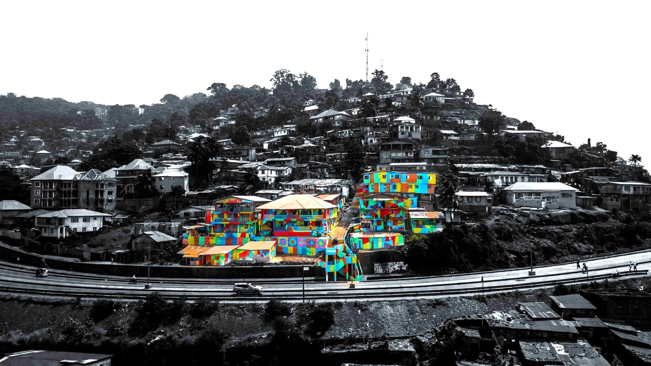 Colorful modern buildings on a hillside in contrast to black and white surrounding neighborhood and landscape.