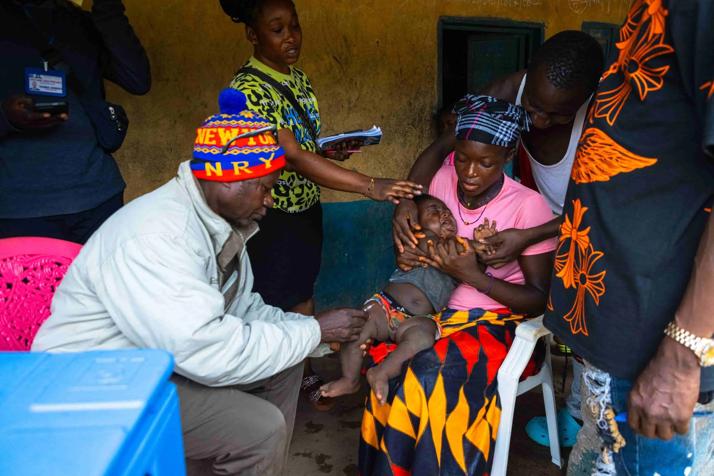 A group of people surrounding a crying child during a medical treatment, with a woman holding the child's head and another person holding the child's arms.