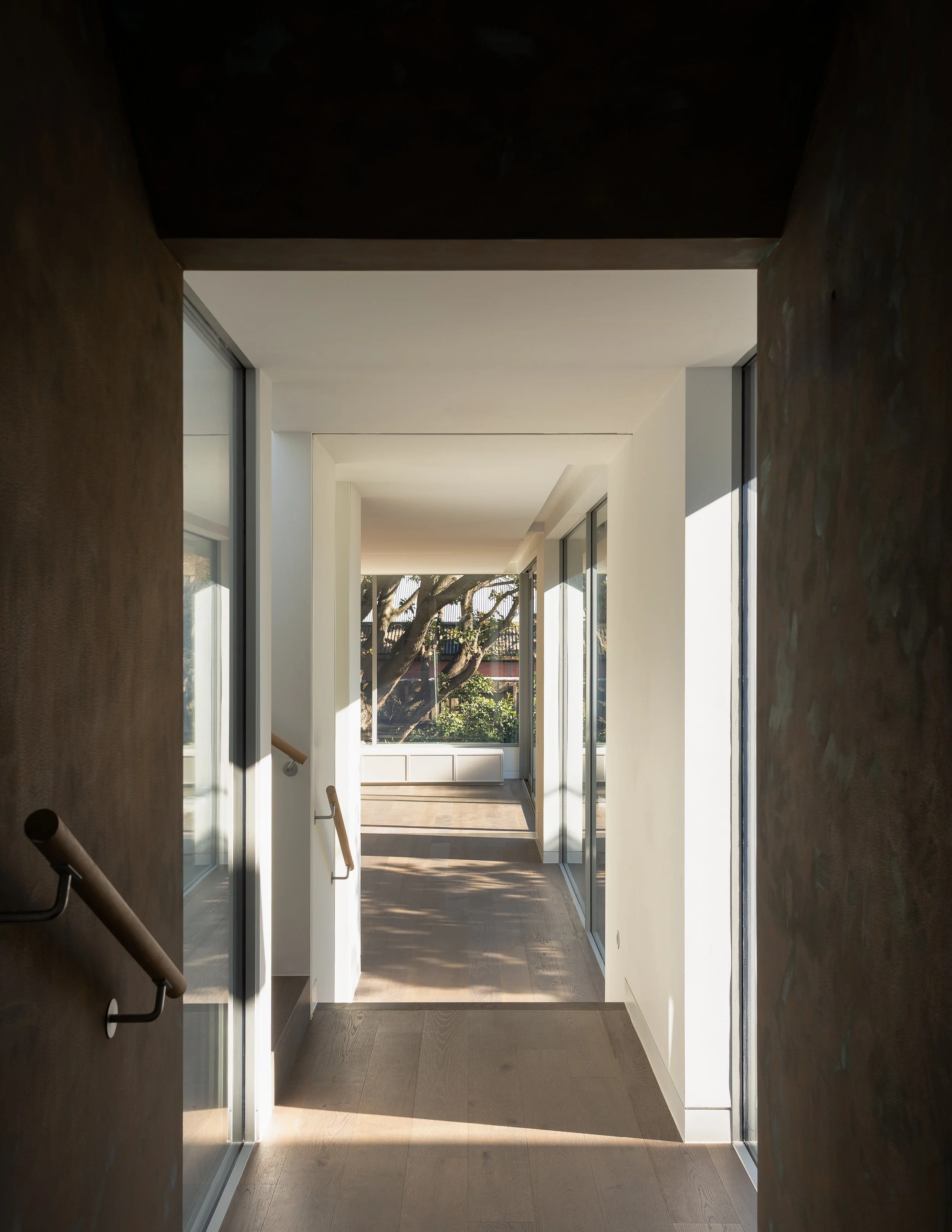 Sunlit modern hallway with glass sliding doors and view of trees outside.