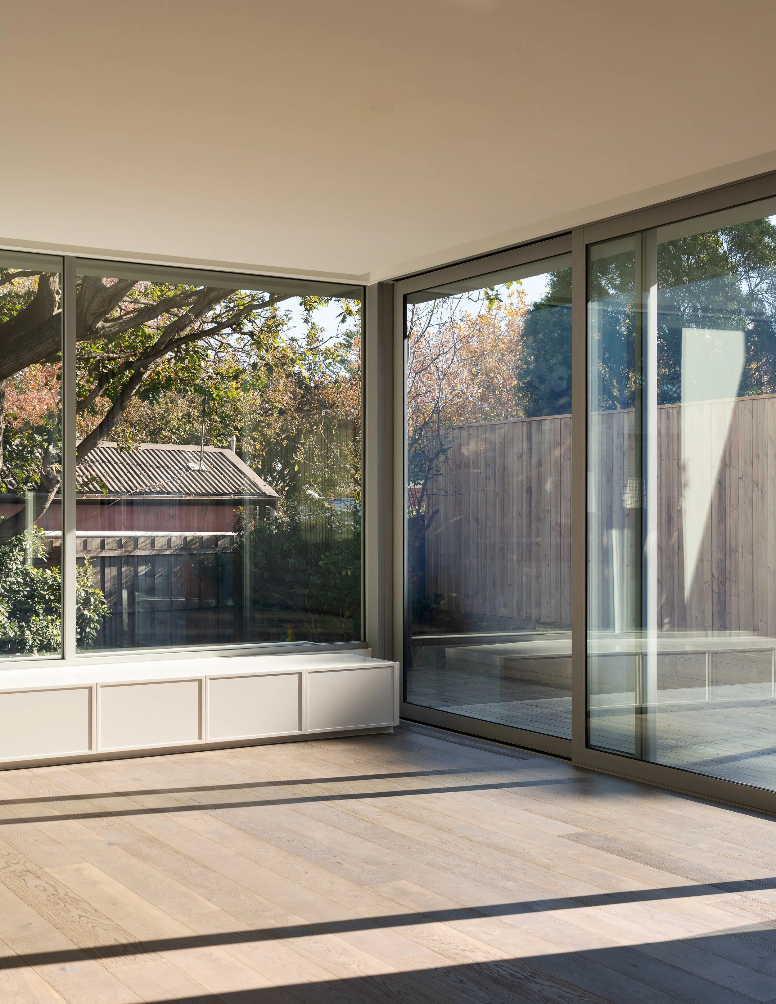 Empty room with large glass sliding doors and a view of a backyard with trees and a wooden fence.