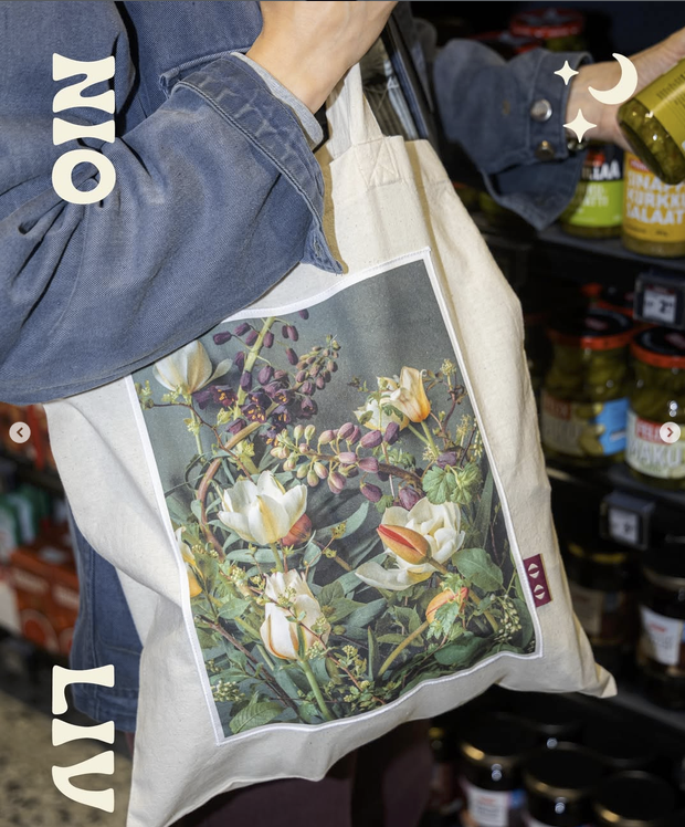 Person holding a tote bag with a floral print, in a grocery store aisle with jars of mustard and other condiments.