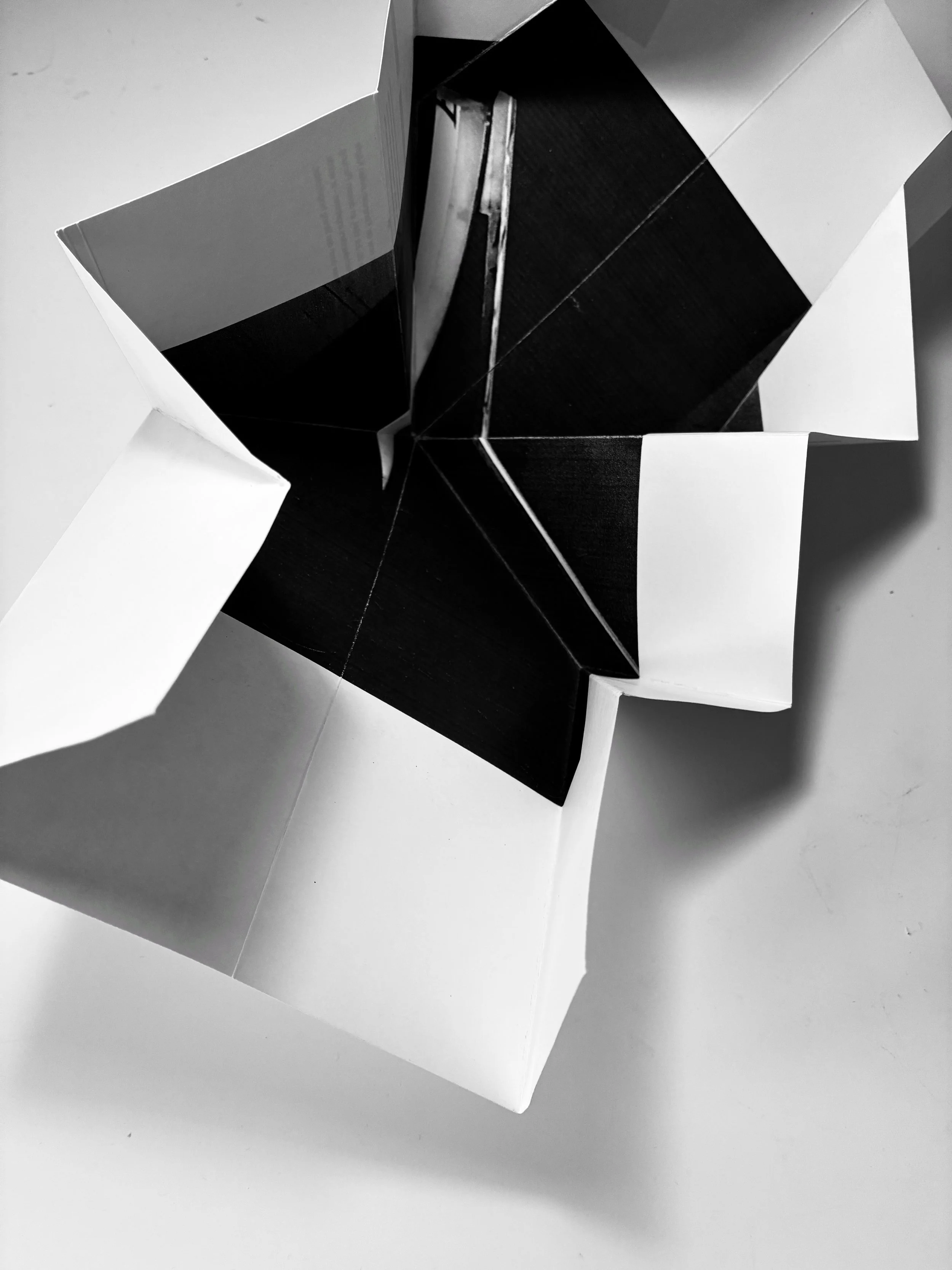Black and white sculpture with geometric shapes, sharp angles, and contrasting white and black surfaces, placed on a white background.