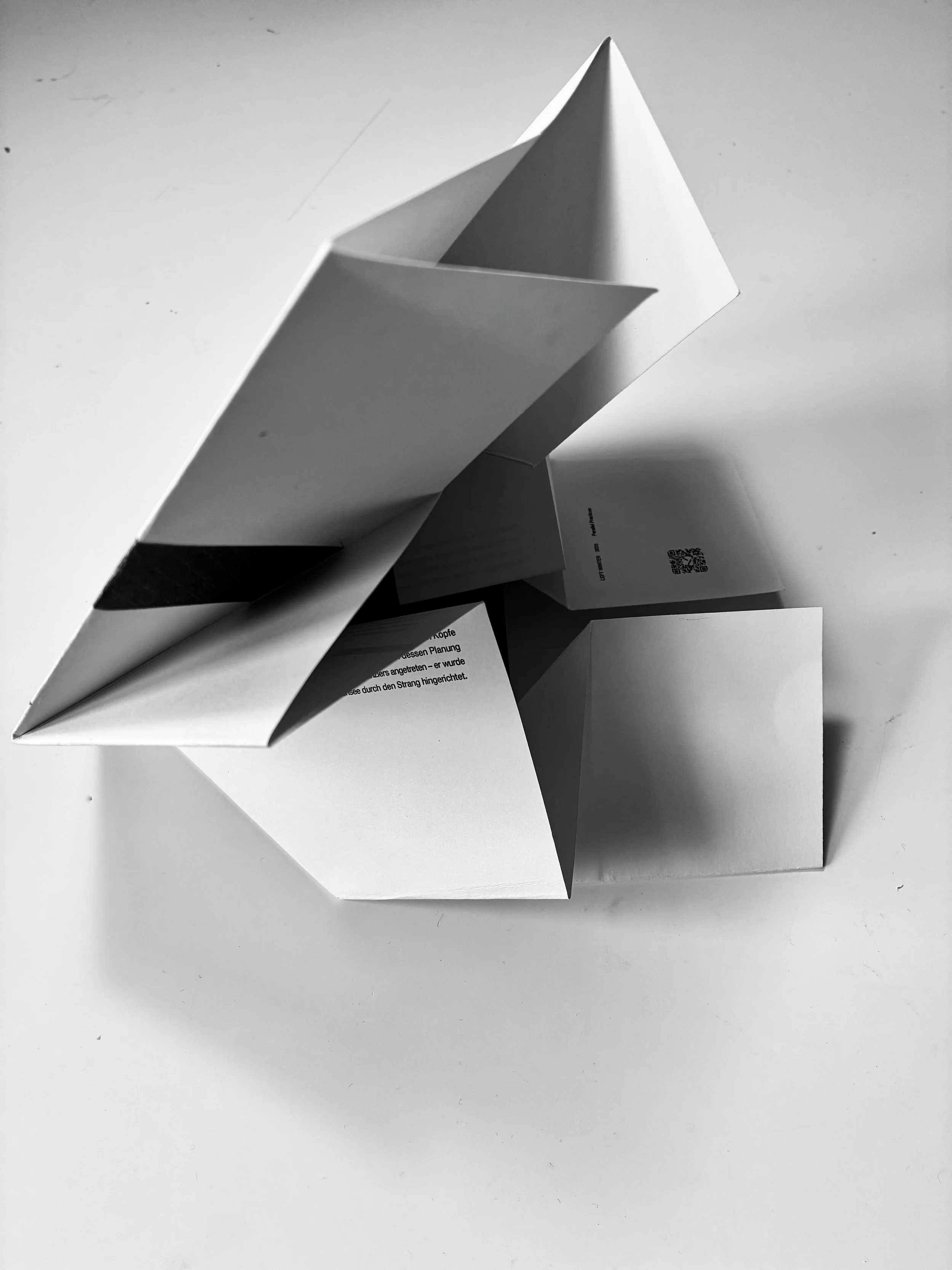 Black and white photo of a paper boat on a flat surface.