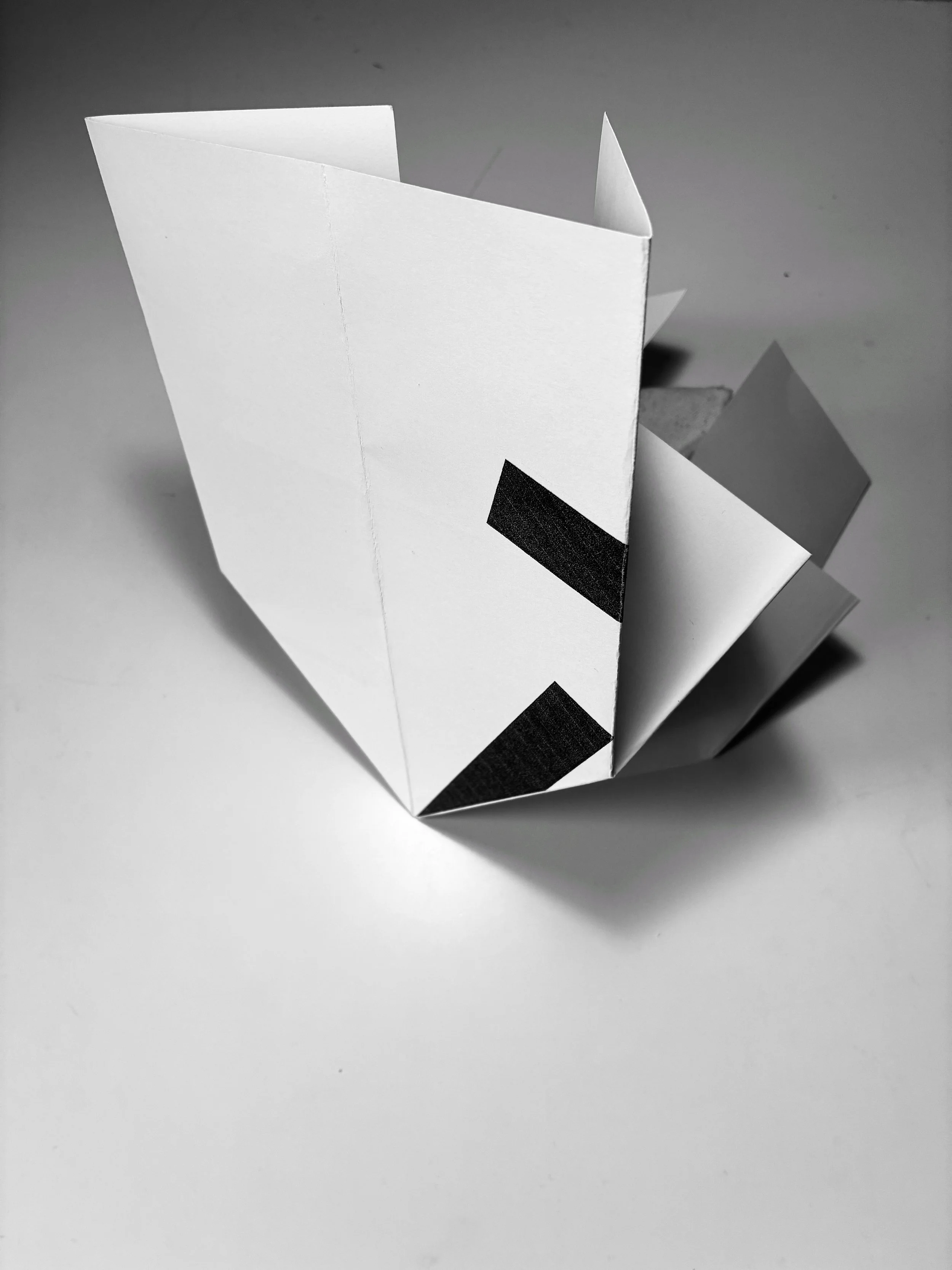Black and white image of a folded paper model with black tape on the edges.