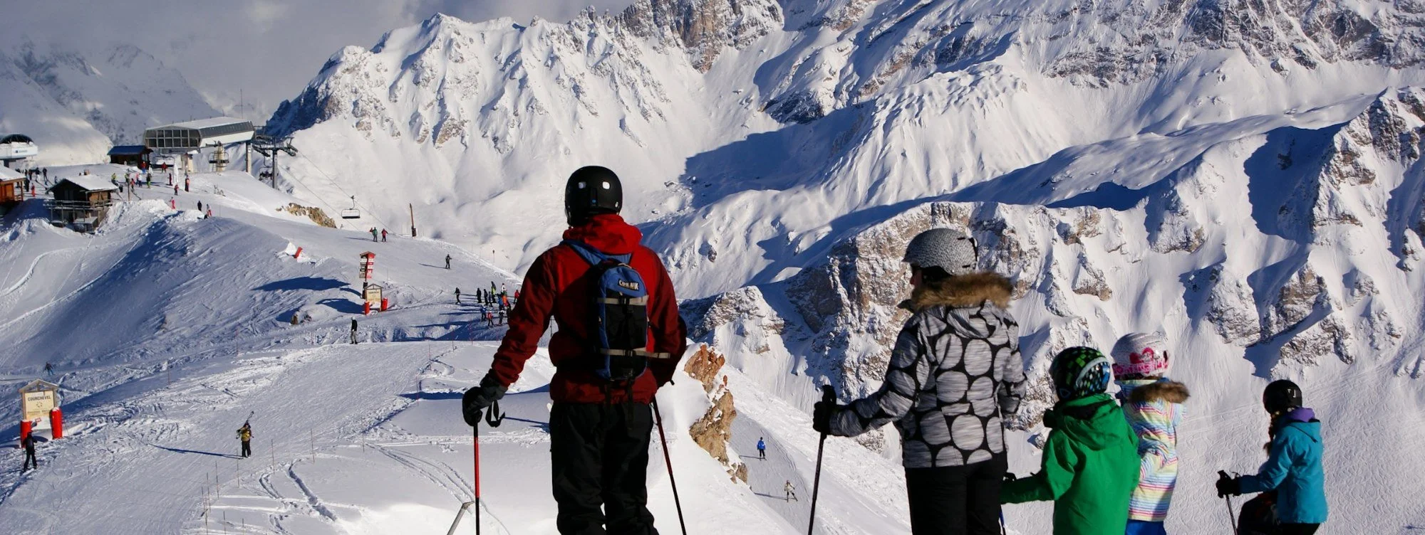 A family of skiers looking out over sunny, snow-covered Alpine peaks