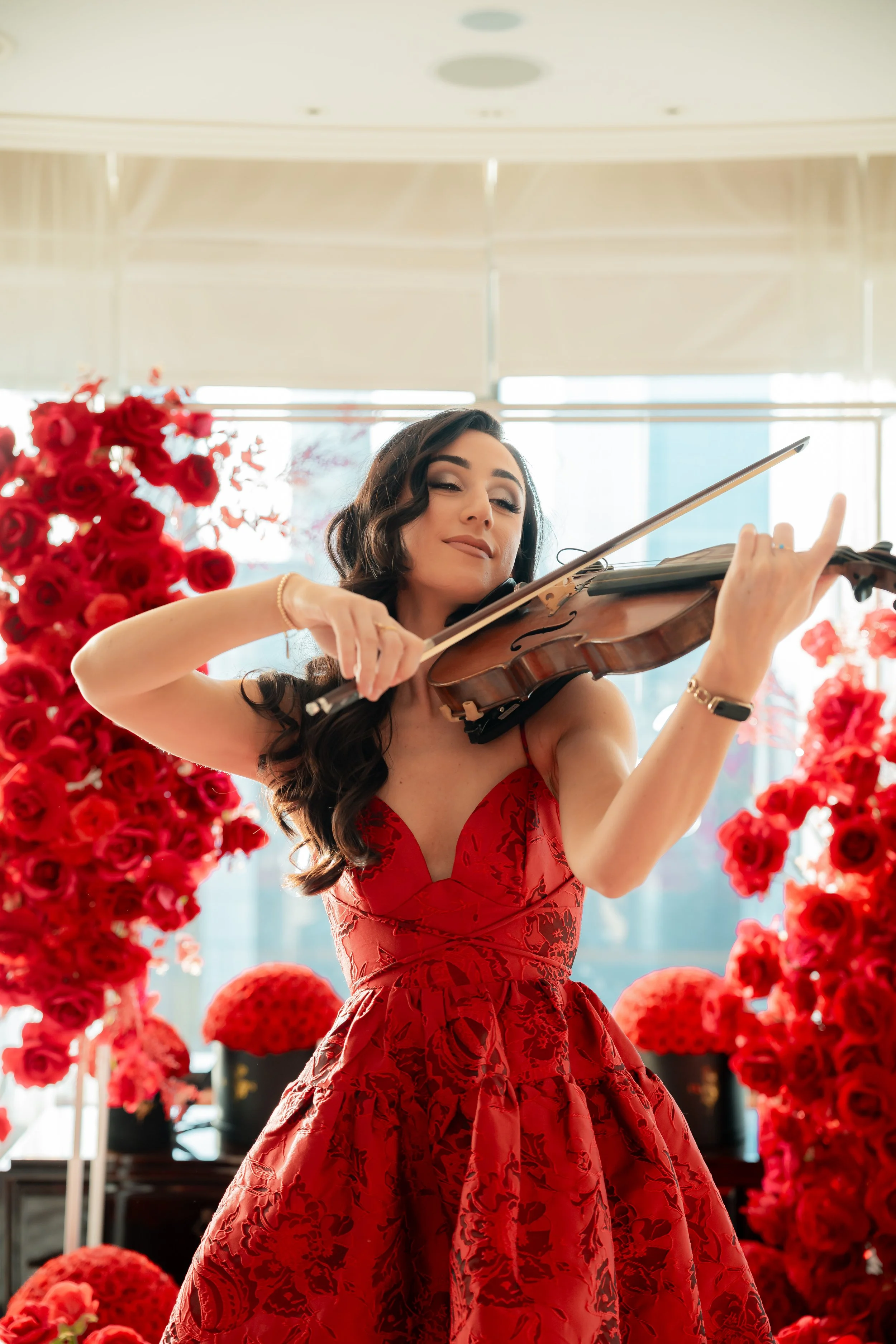 Evangeline Victoria performs passionately on her violin during a romantic proposal at Crown Casino Melbourne, wearing a stunning red gown and surrounded by vibrant red roses, enhancing the magical moment.