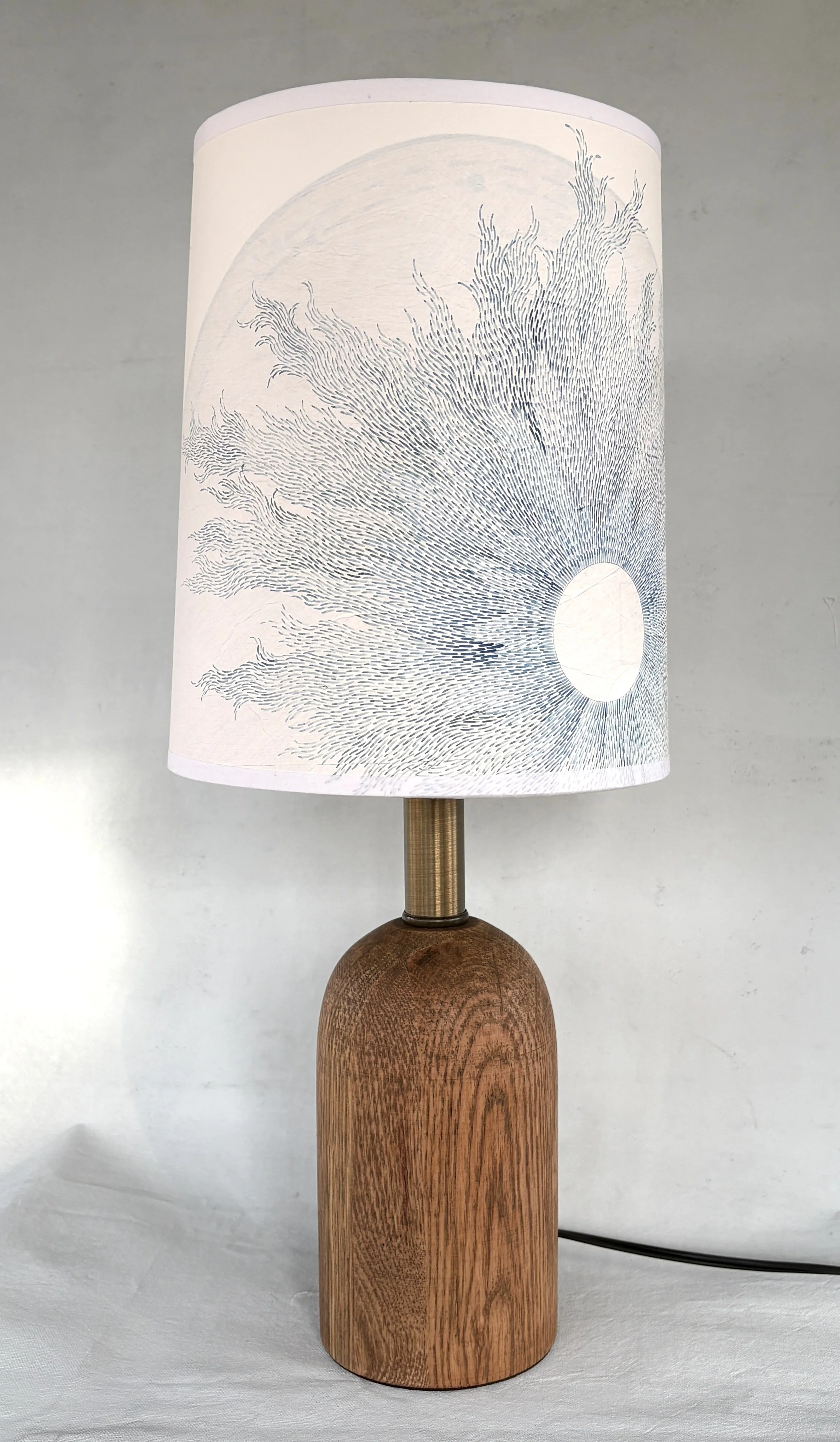Decorative table lamp with a wooden base and a white lampshade featuring a delicate, abstract line art design resembling flowing waves.