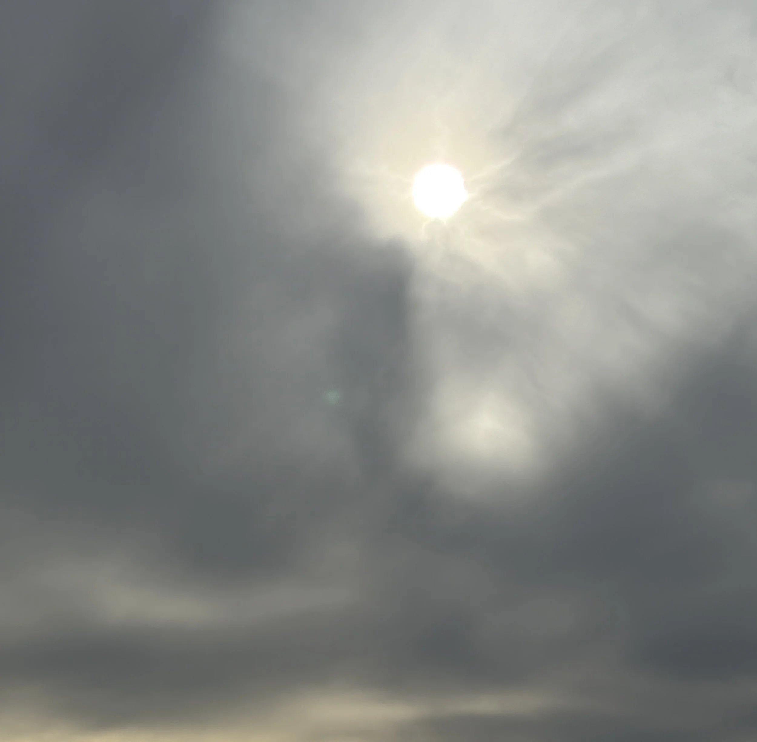 The sun partially obscured by cloudy sky with rays shining through.
