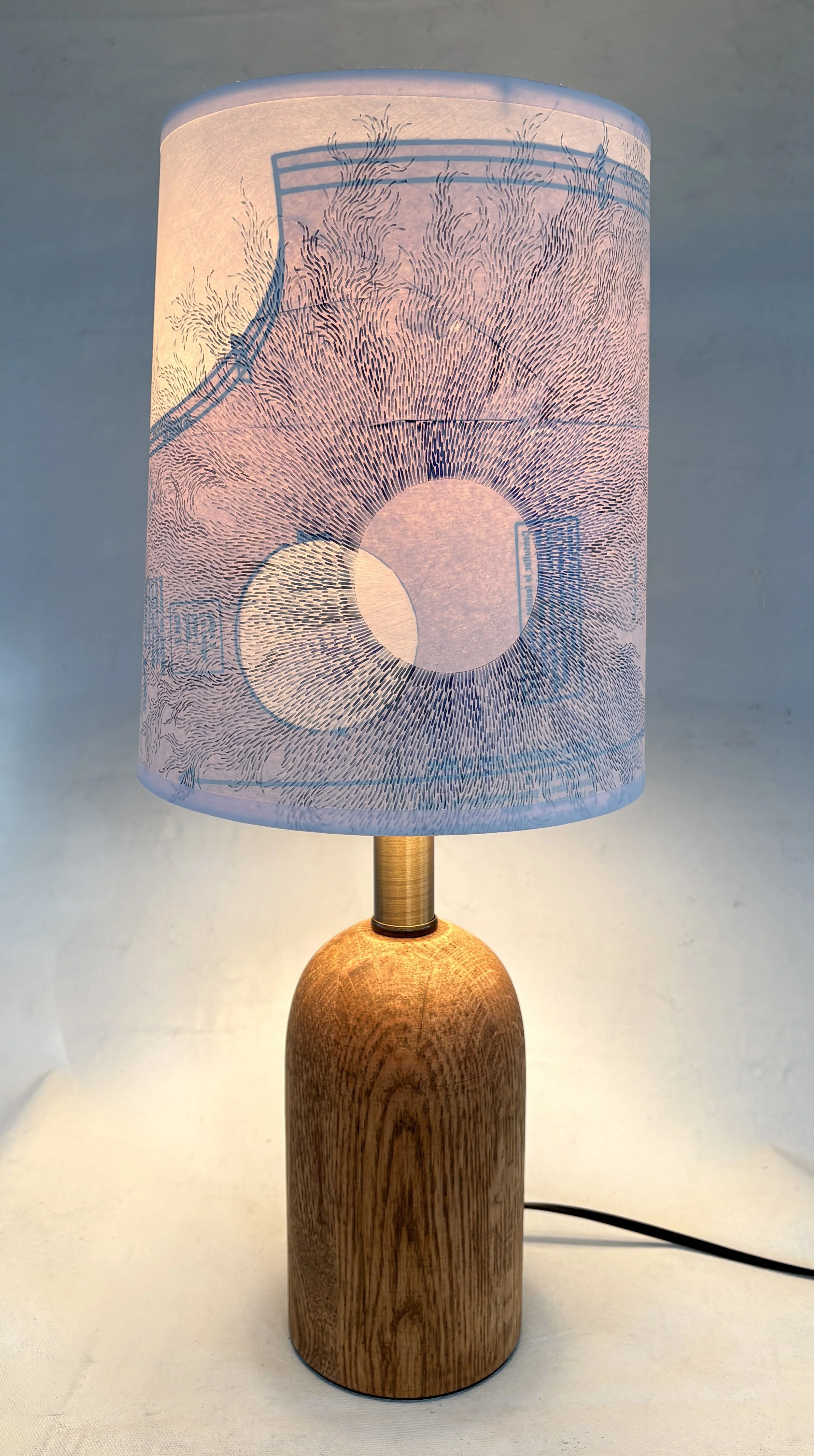 Decorative table lamp with a wooden base and a white handpainted lampshade featuring a delicate, abstract line art design resembling flowing waves.