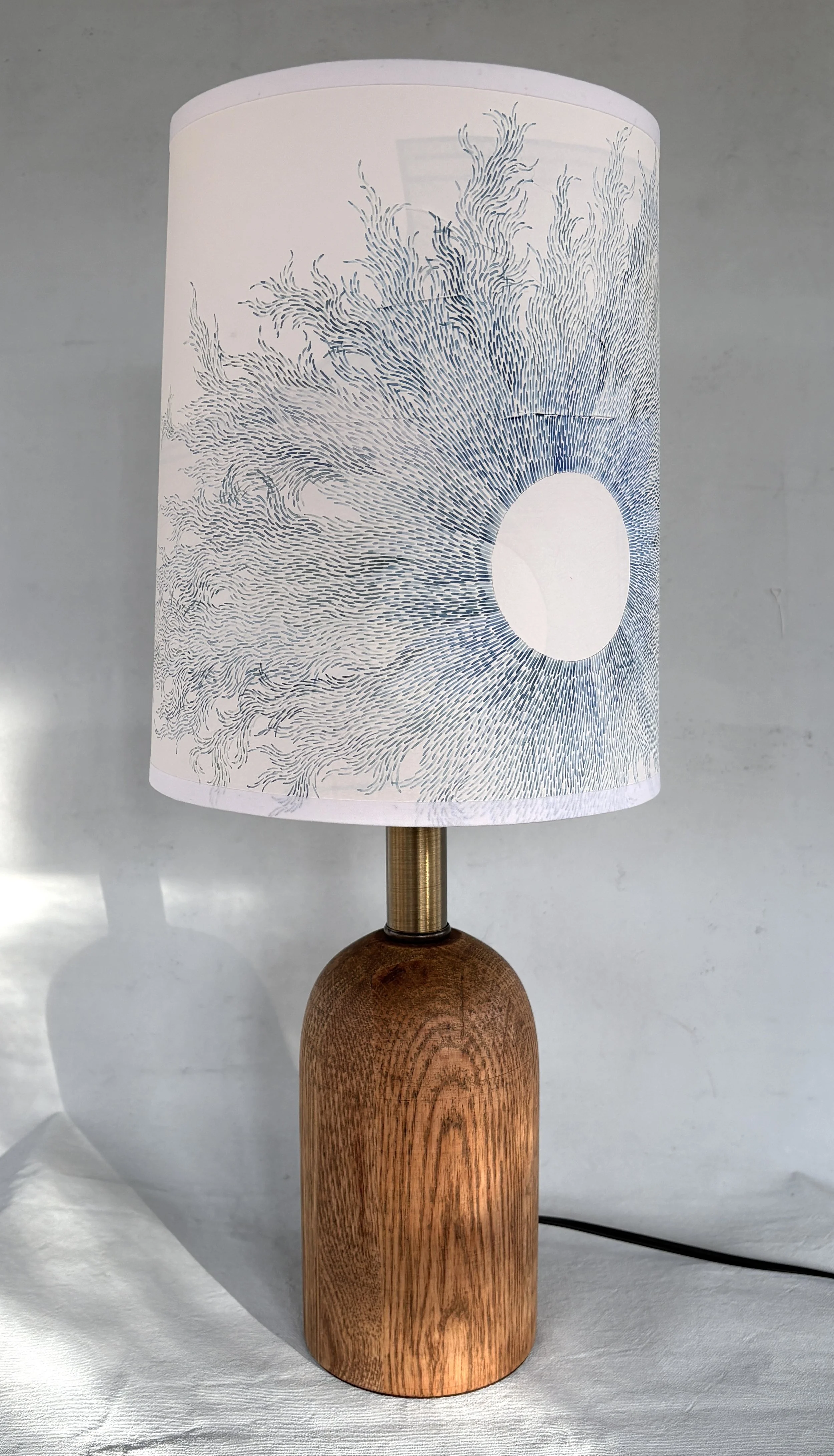 A table lamp with a white hand painted lampshade featuring a blue abstract design resembling flowing water