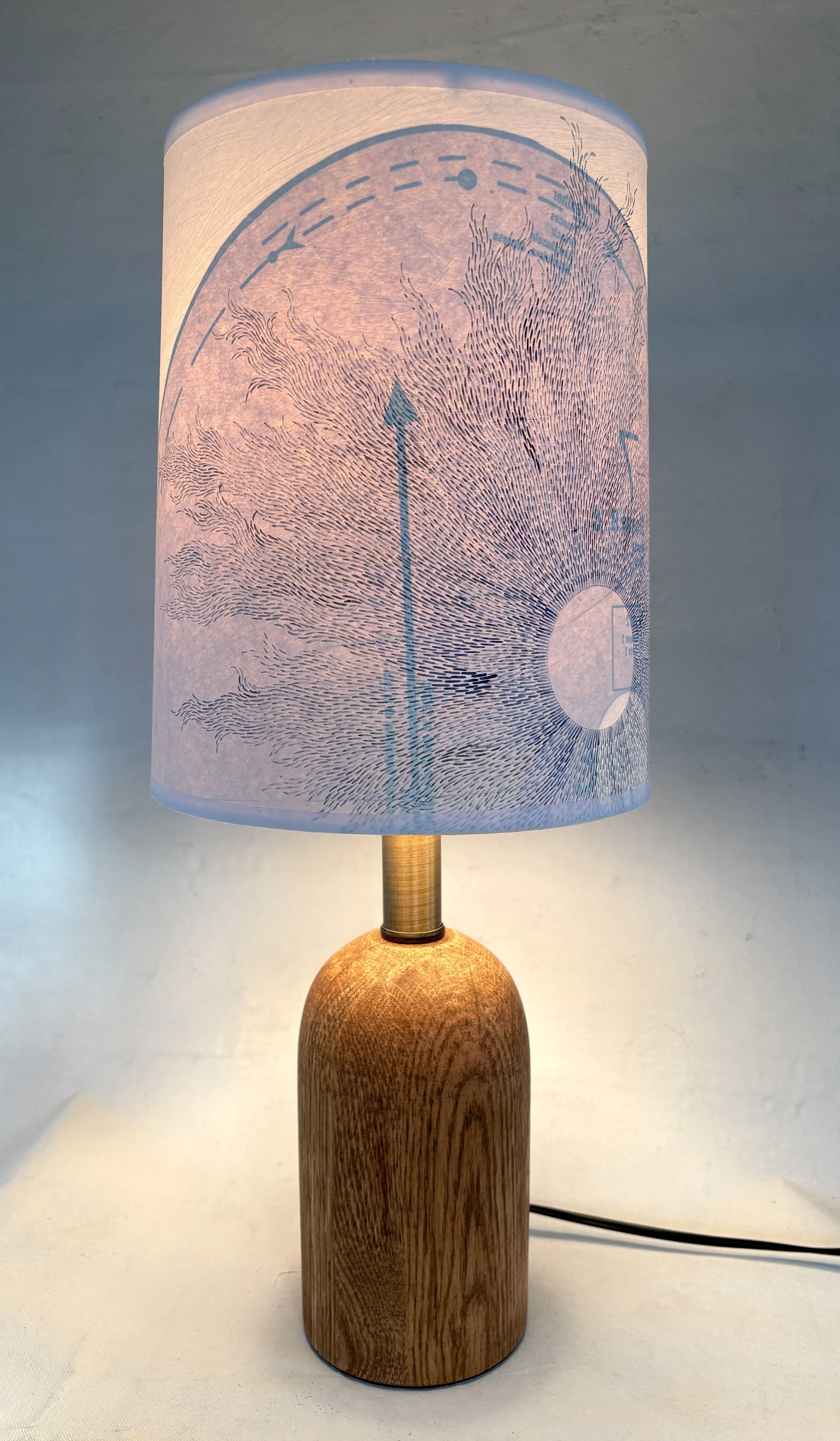 A table lamp with a cylindrical wooden base, a bespoke handpainted paper shade of artistic lines.