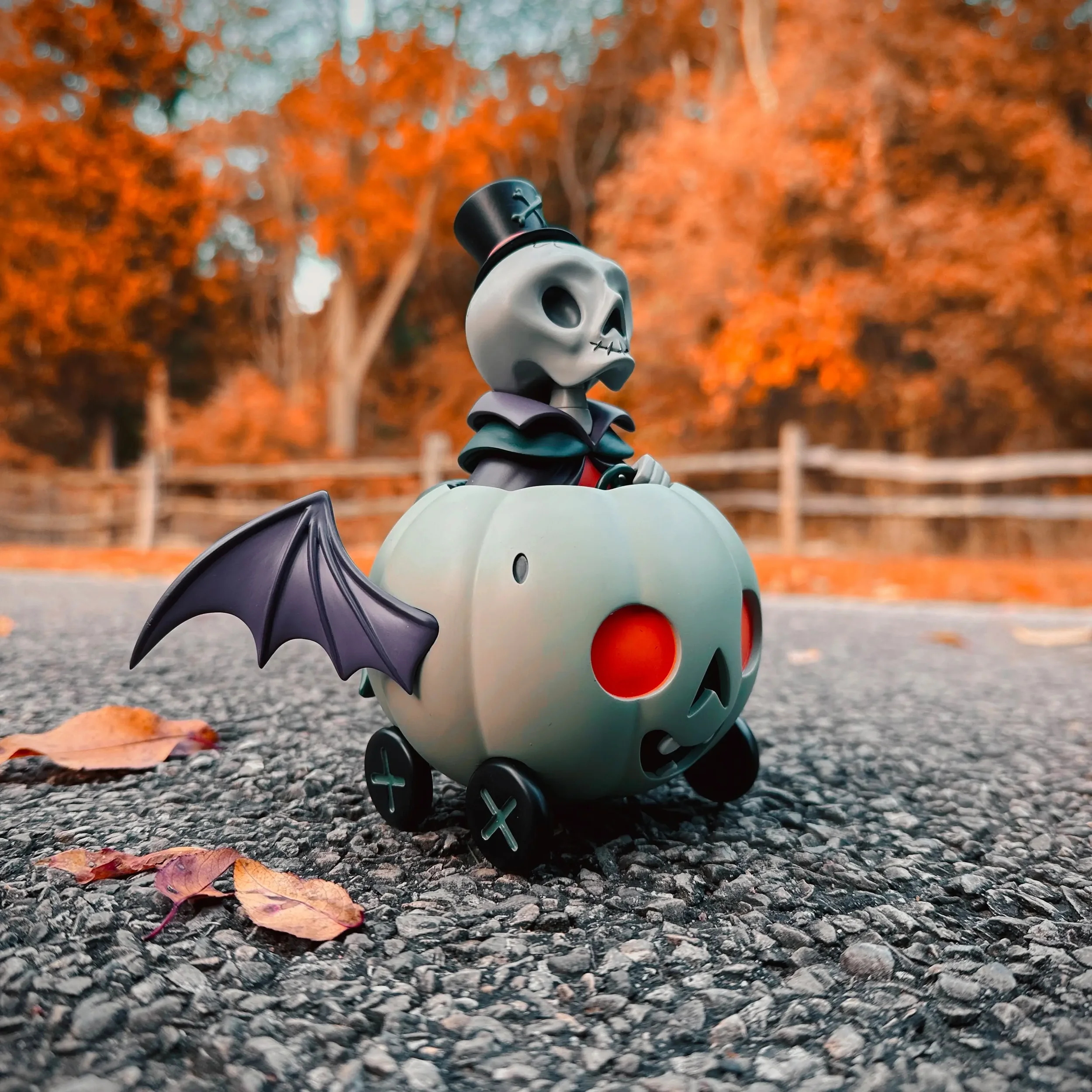 Stephanie Buscema Nigel the Necromancer resin art toy on autumn pavement with fallen leaves and rustic fence background