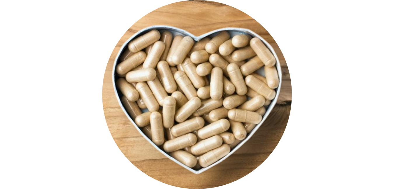 A heart-shaped container filled with beige capsules on a wooden surface.