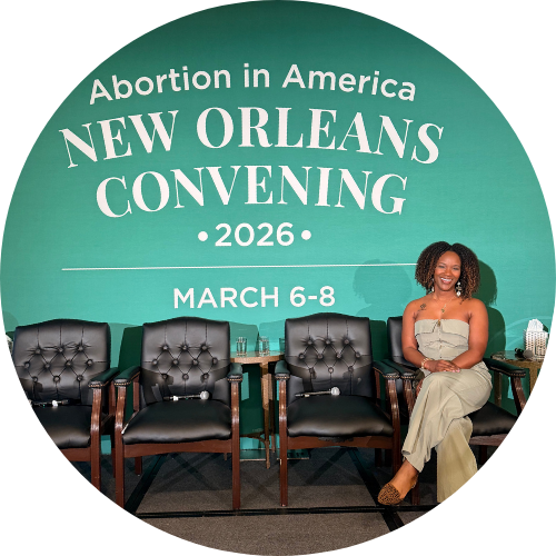 A woman sitting on a chair at the Abortion in America New Orleans Convening 2026, with a green backdrop displaying event details from March 6-8.