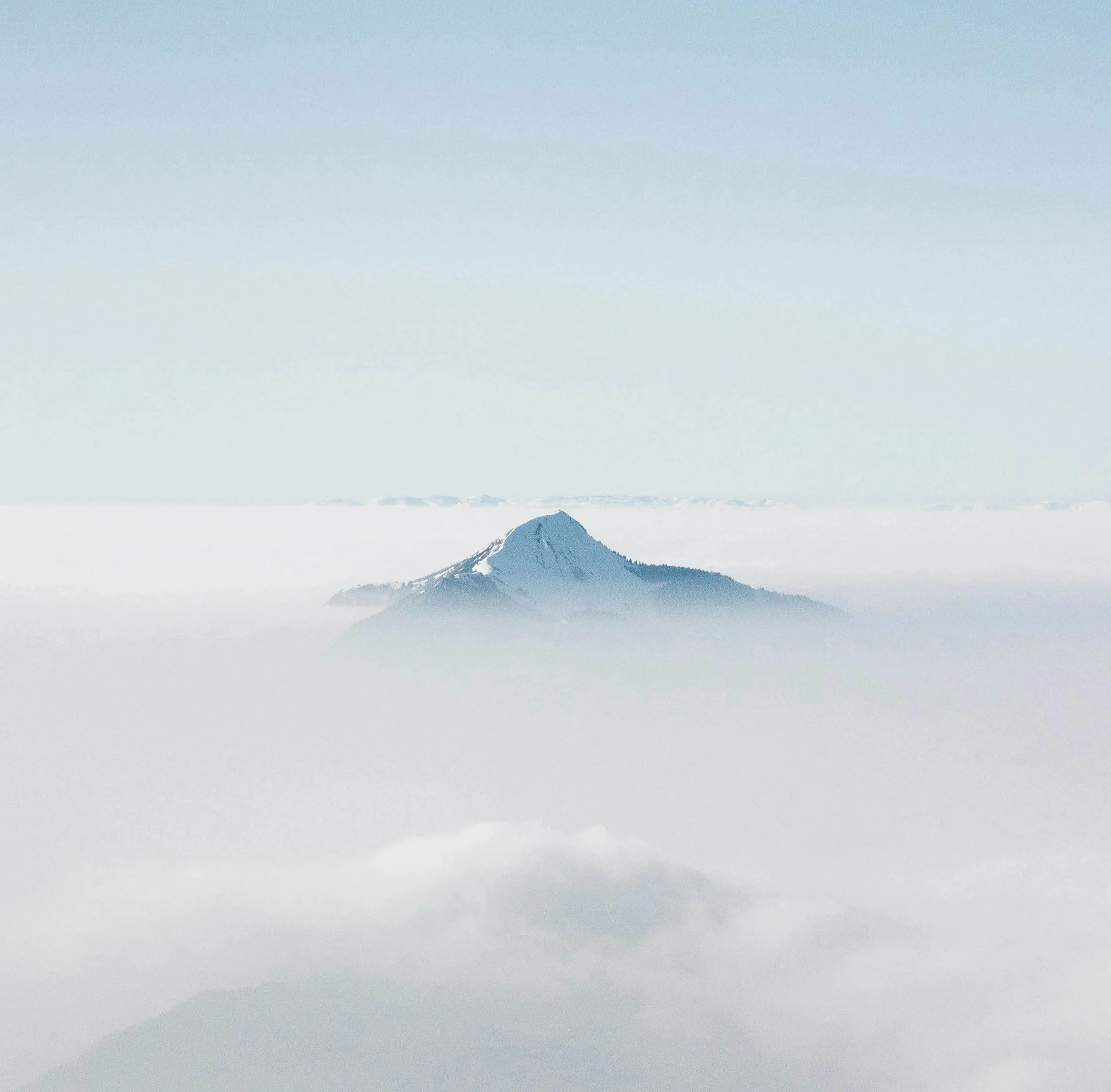snowy mountain peak poking out of white clouds against a blue sky