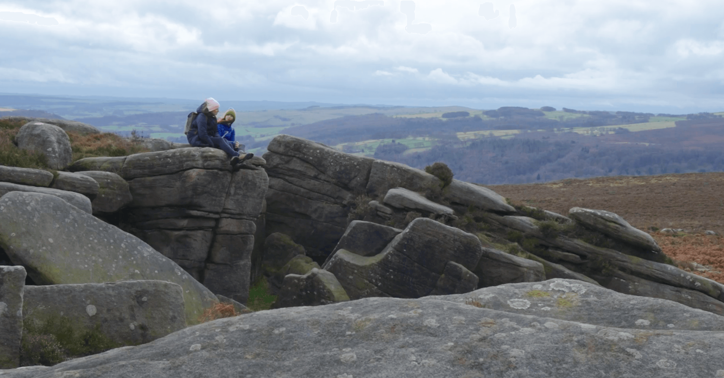 Katie Newman and a client sat on large rocks in The Peak District, talking, under a cloudy sky.