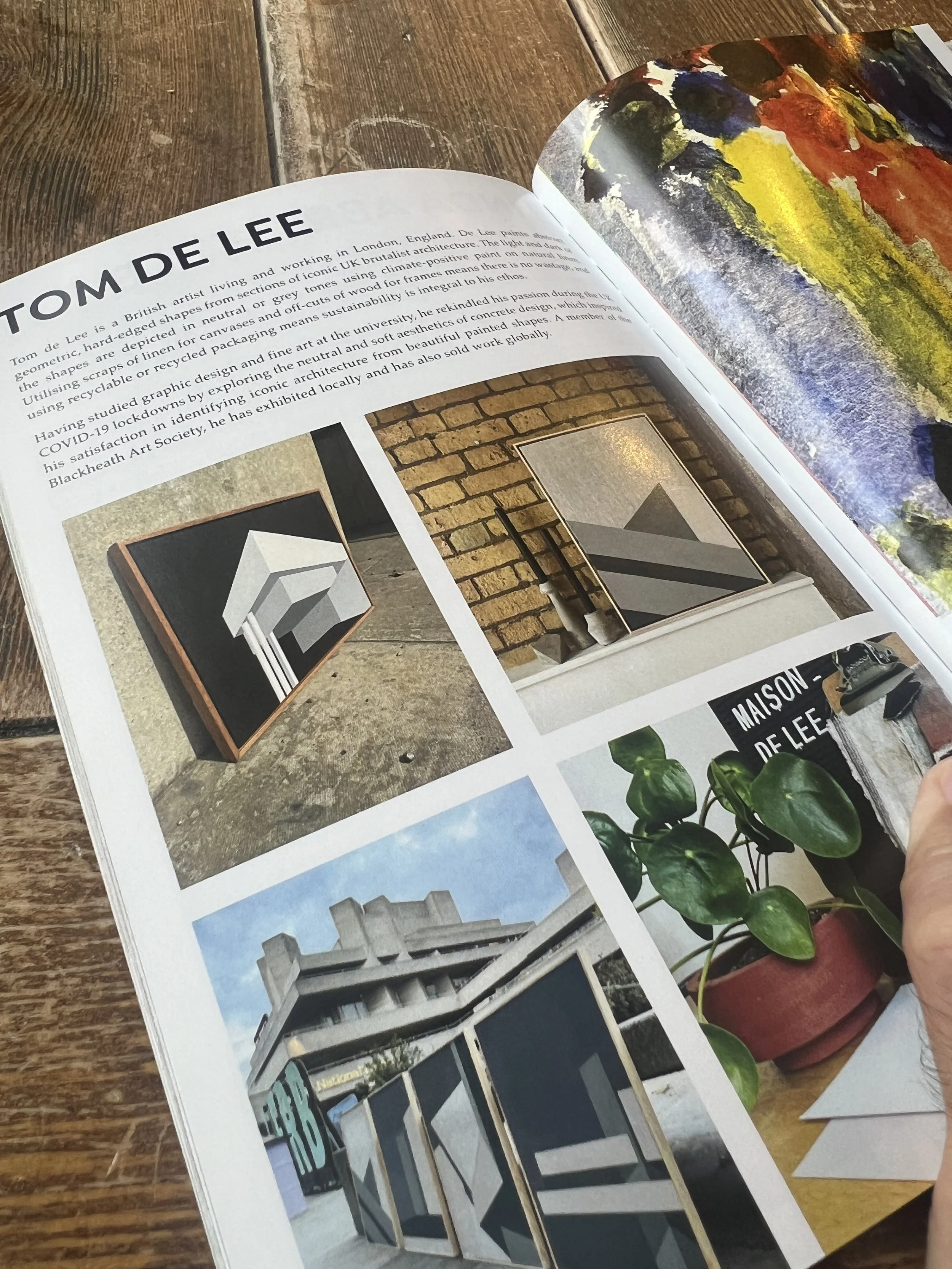 Open magazine displaying articles and images about architecture, including modern buildings, interior designs, and artwork, on a wooden surface.