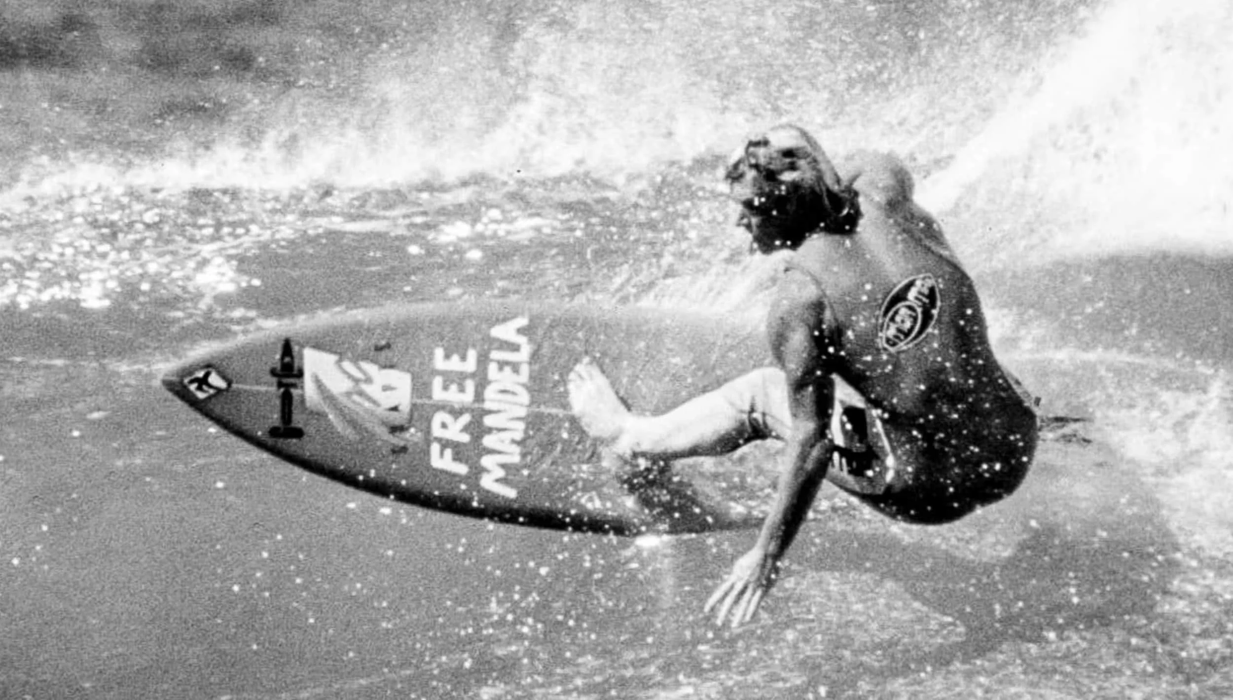 A surfer riding a wave on a surfboard that has the words 'FREES WORLD' written on it, while wearing goggles and a wetsuit.