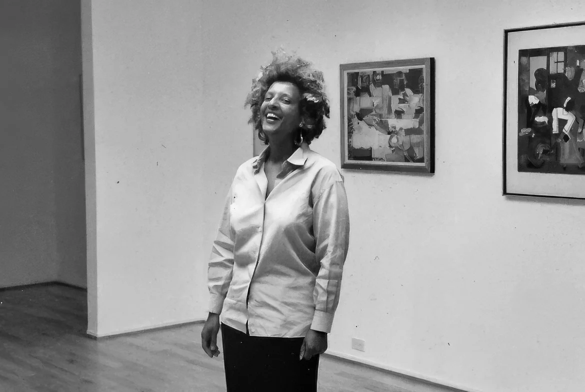 Five people standing together in an art gallery, smiling at the camera, with framed artwork on the wall behind them.