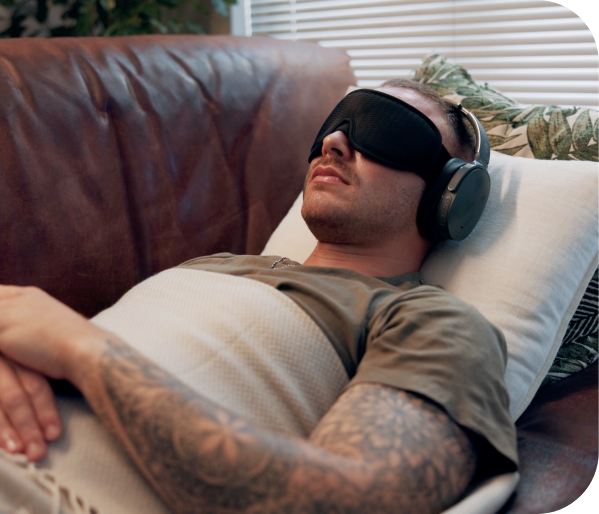 Man lying on a couch with a sleep mask and headphones, relaxing with eyes closed.