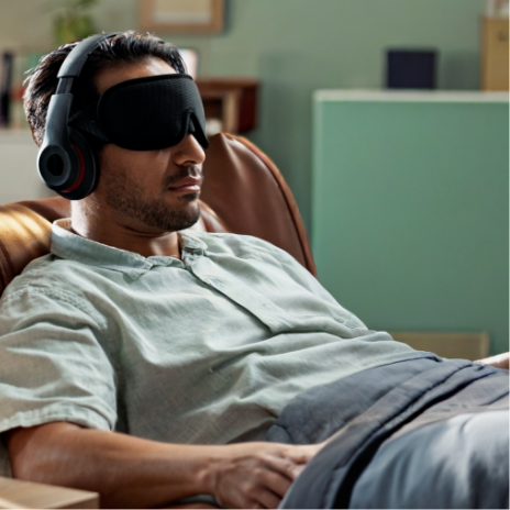 Man lying on a couch wearing an eye mask and headphones.