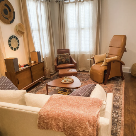 Cozy living room with beige sofa, brown leather armchairs, wooden coffee table, and large window with curtains.