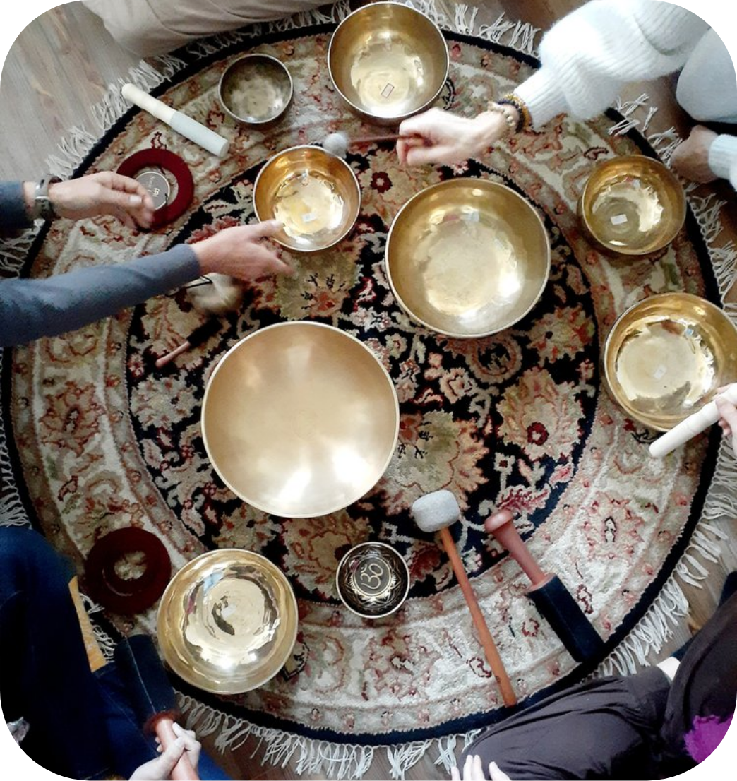 People playing crystal singing bowls on a colorful, patterned rug indoors.