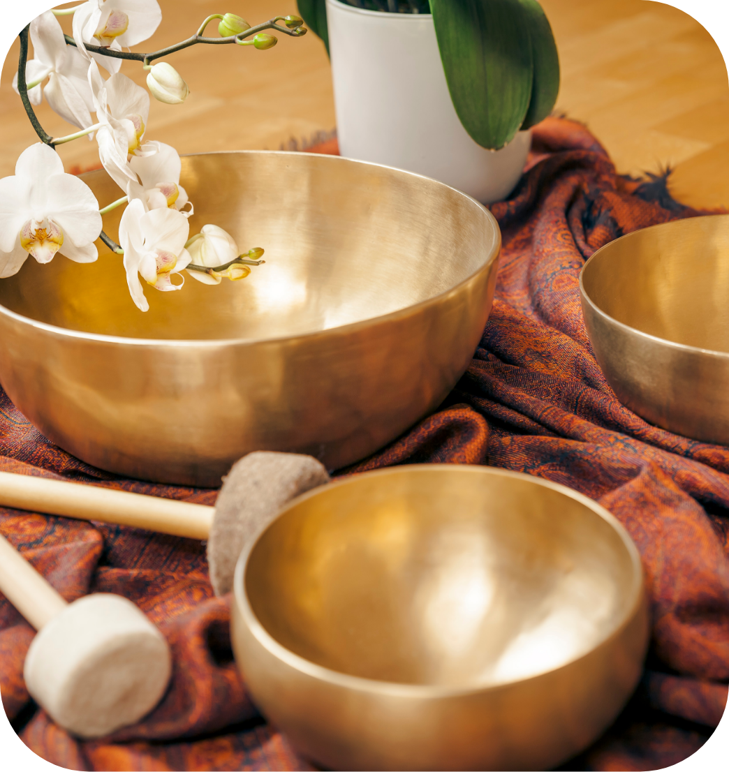 Three metallic singing bowls arranged on a patterned cloth, with a white orchid plant and a potted green plant in the background.