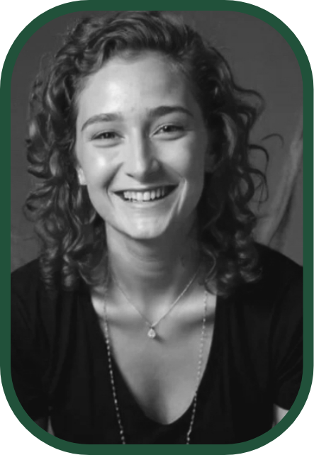 A young woman with curly hair smiling at the camera, wearing a necklace and a dark top, in a grayscale photo.