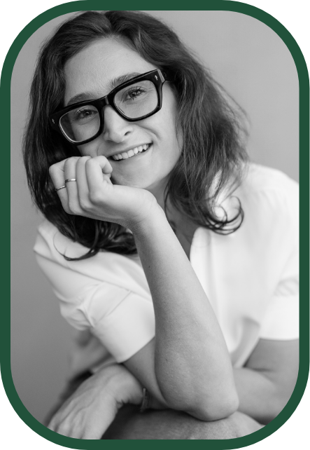 A young woman with curly hair smiling at the camera, wearing a necklace and a dark top, in a grayscale photo.