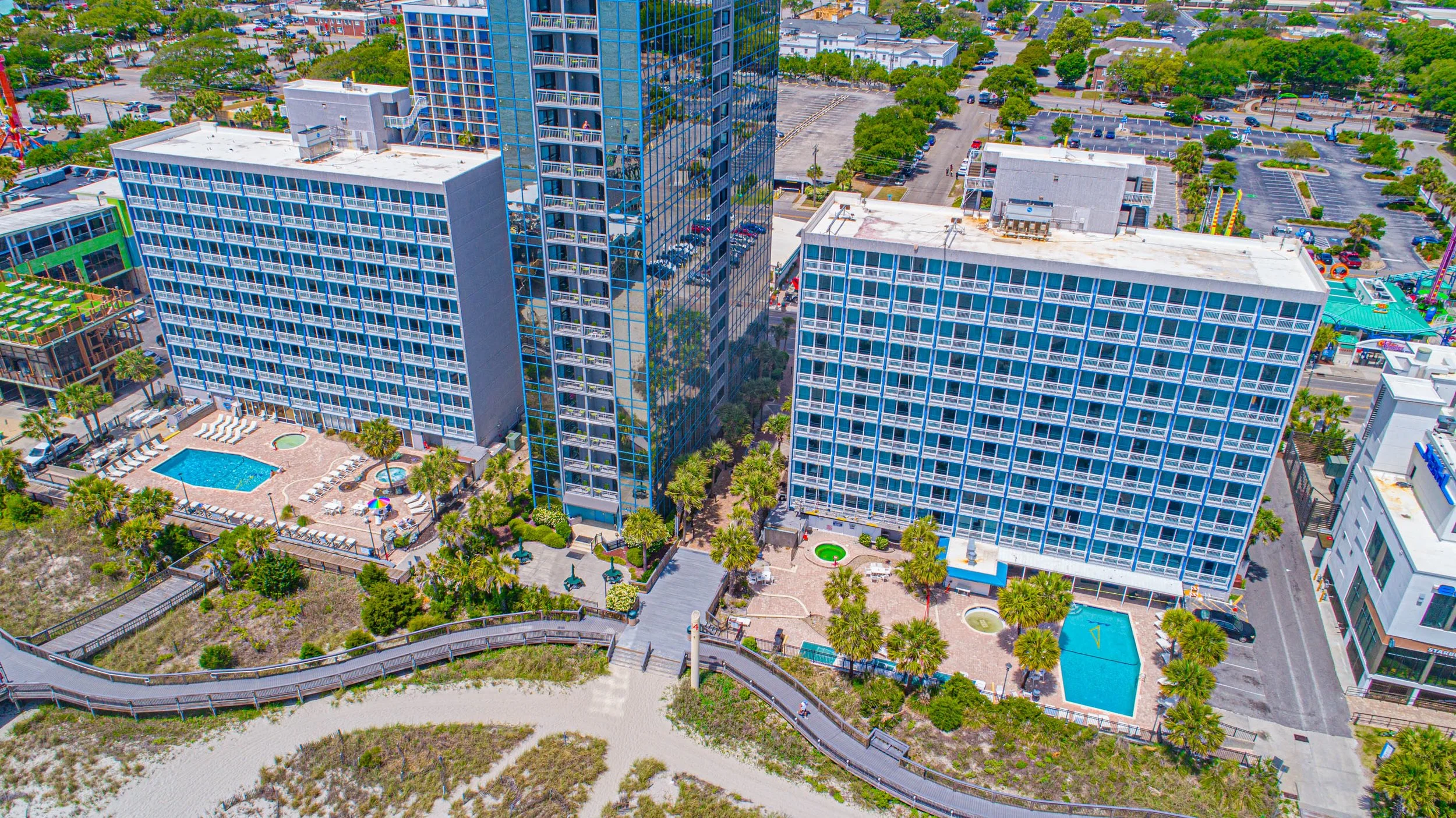 Aerial view of high-rise buildings in a city with swimming pools, outdoor seating areas, parking lots, and surrounding greenery.