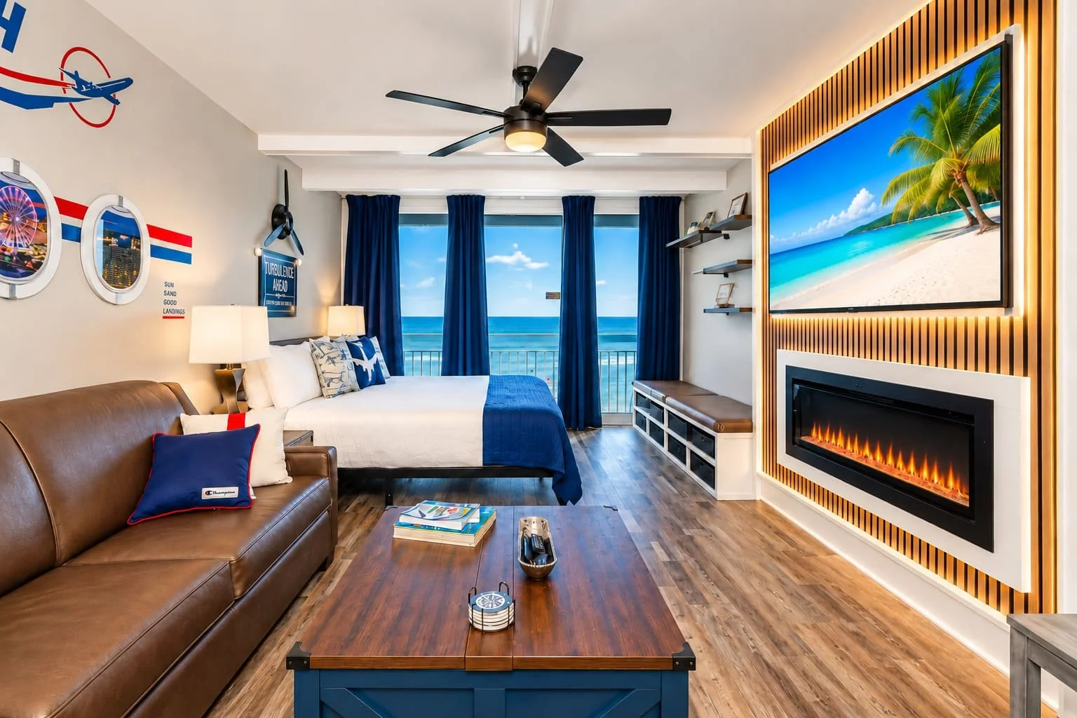 Beach view from a hotel room window with ocean, blue sky, and palm trees, interior with blue and white decor, leather couch, TV, fireplace, and wooden furniture.