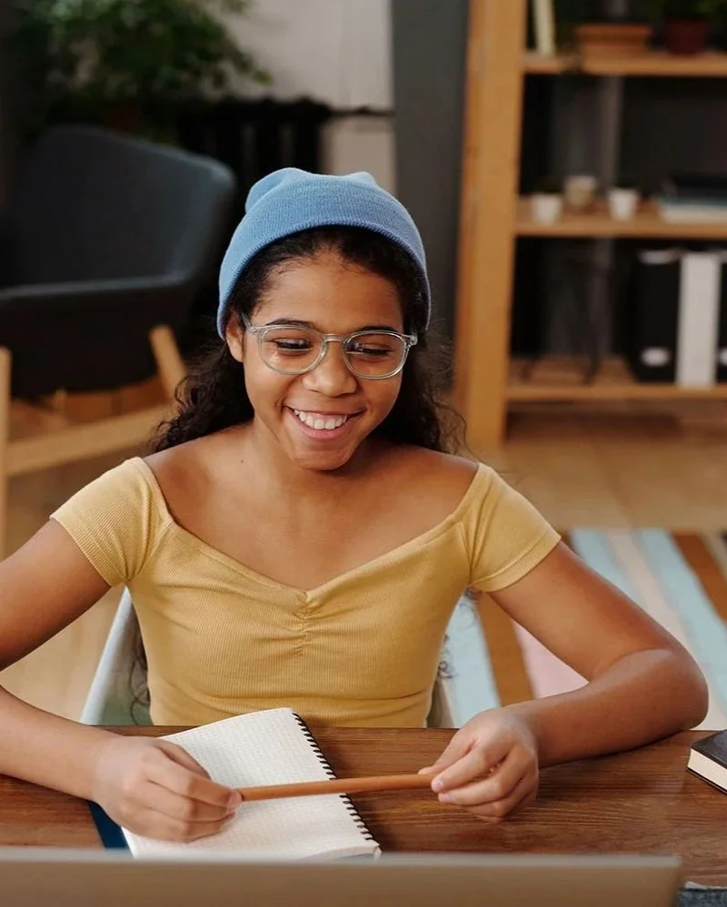 Young player smiles at her laptop with a notebook and pencil during D&D night.