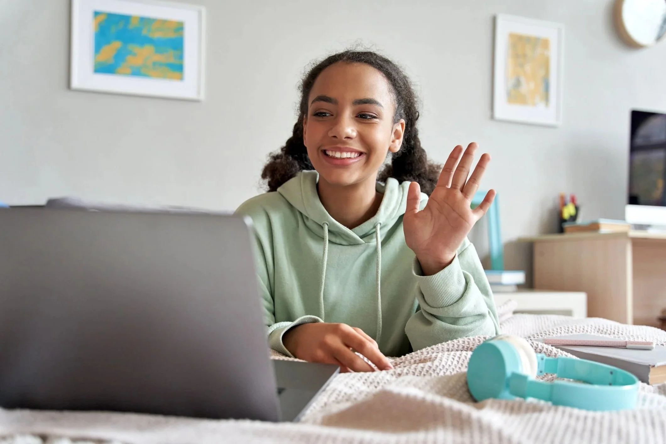 A smiling teenage girl waves at her fellow online DND players on her laptop.