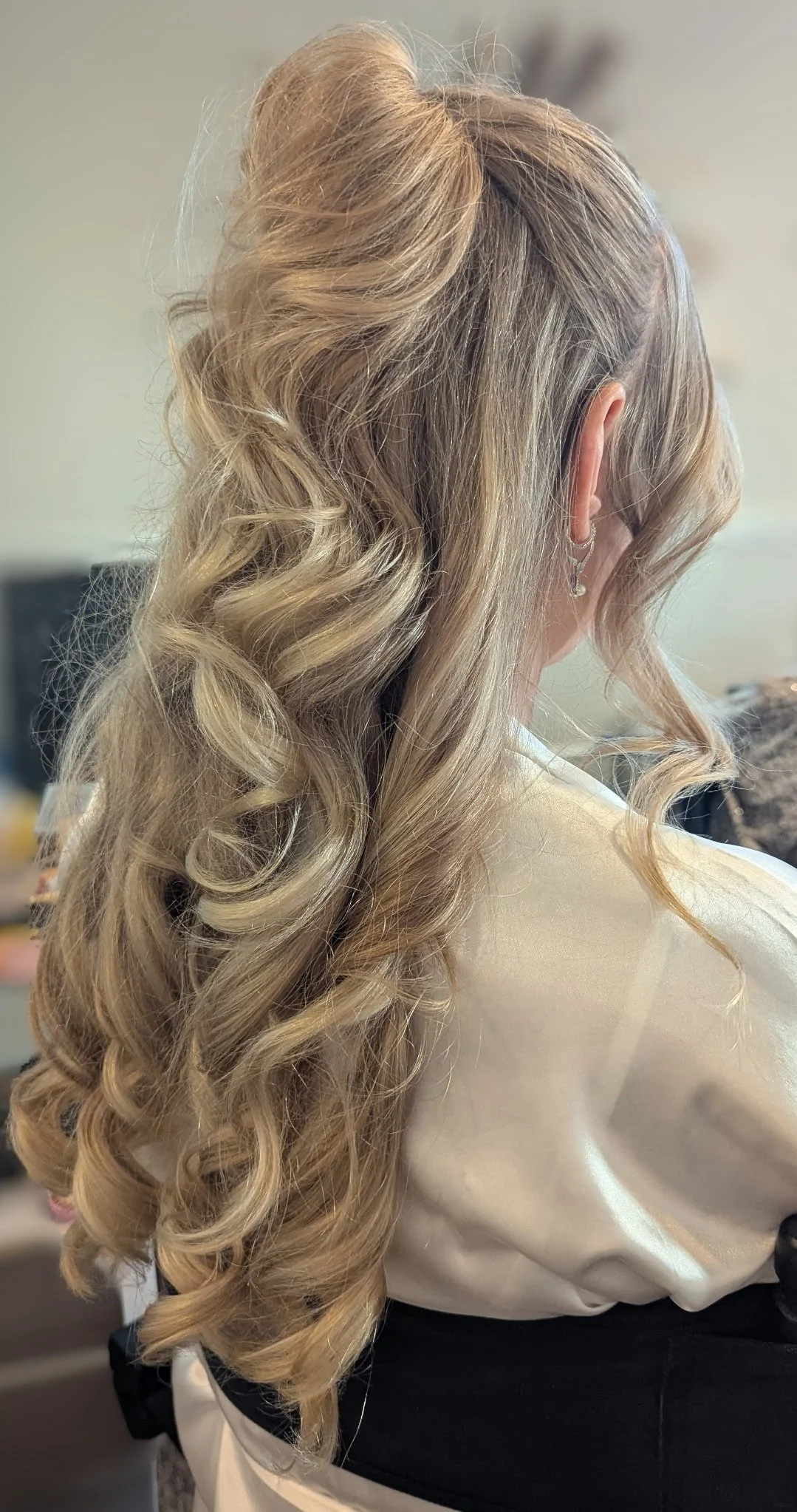 Blonde woman with long, curled hair and wearing earrings, seen from the side.