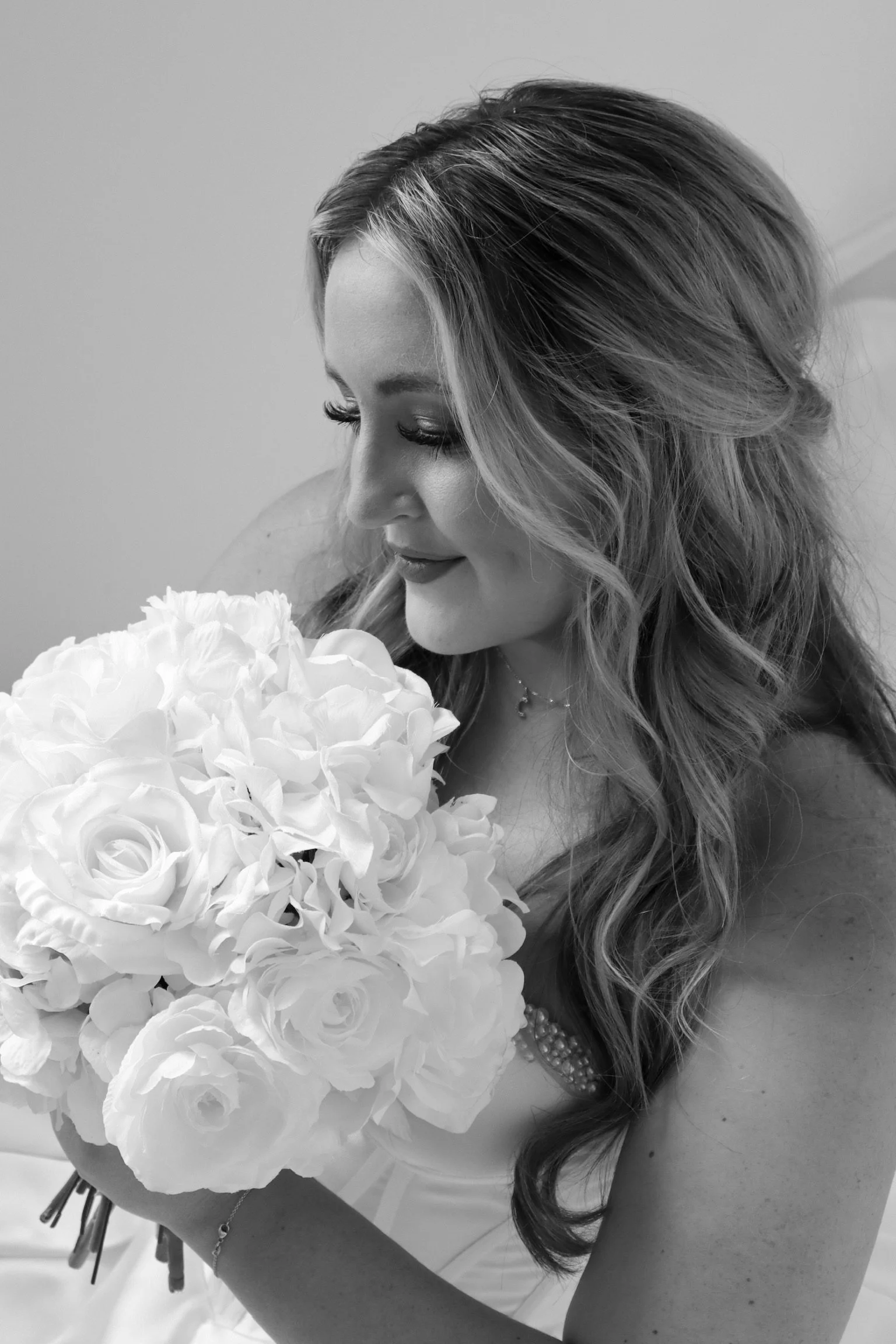 A black and white photo of a woman with long, wavy hair holding a bouquet of roses, looking down at the flowers.